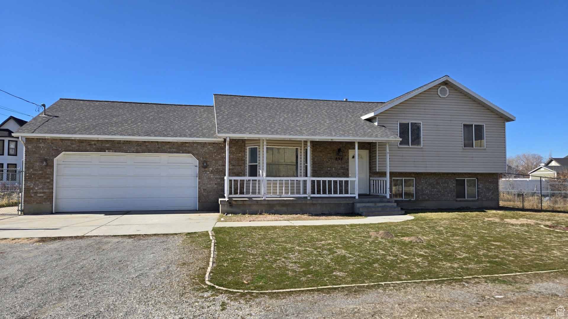 Split level home featuring a porch, concrete driveway, an attached garage, a shingled roof, and brick siding