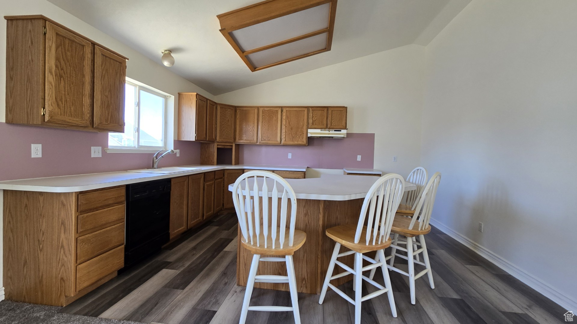 Kitchen featuring a kitchen island, under cabinet range hood, dishwasher, lofted ceiling, and a sink