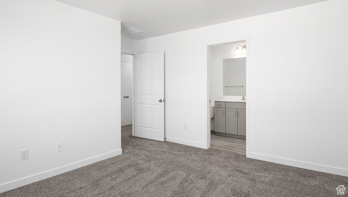 Unfurnished bedroom with ensuite bath, a textured ceiling, baseboards, and carpet