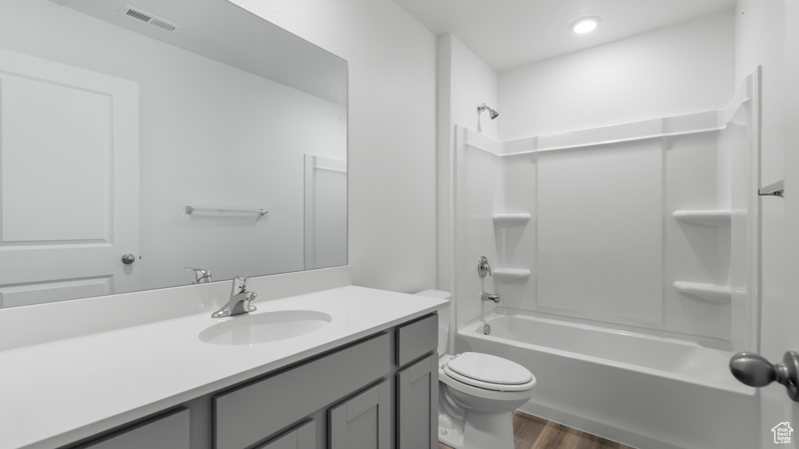 Bathroom with vanity, wood finished floors, visible vents, shower / tub combination, and toilet