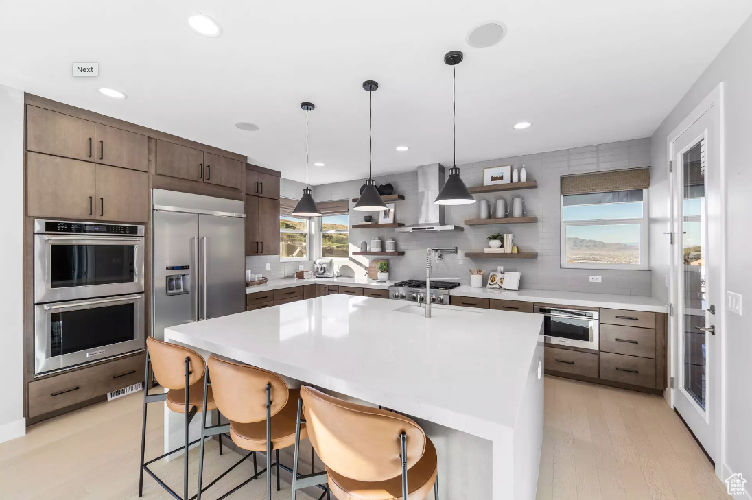 Kitchen with open shelves, stainless steel appliances, wall chimney exhaust hood, light countertops, and decorative backsplash