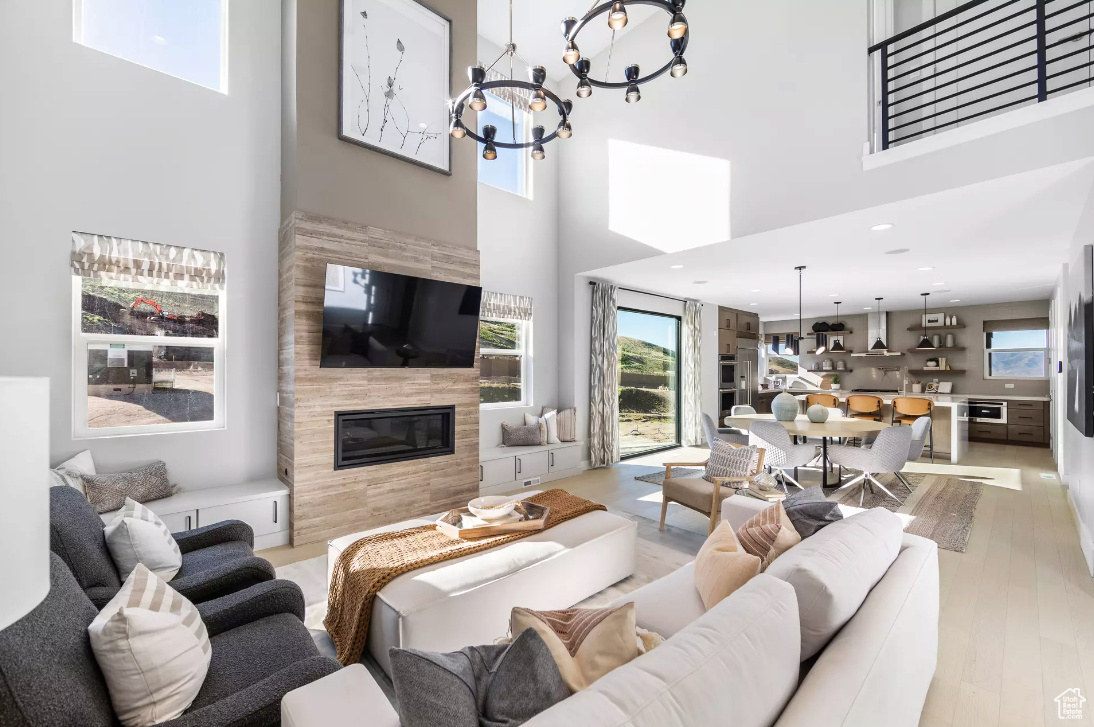 Living room with a chandelier, light wood-type flooring, recessed lighting, a fireplace, and a towering ceiling