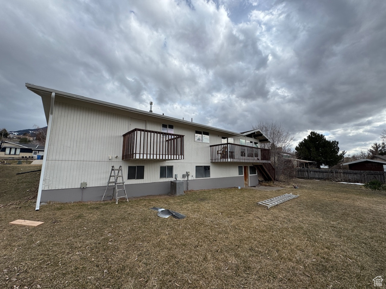 Rear view of house with a yard, central AC unit, stairs, and fence