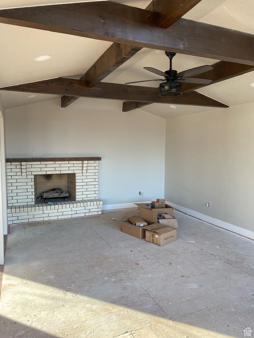 Unfurnished living room with lofted ceiling with beams, baseboards, a brick fireplace, and ceiling fan