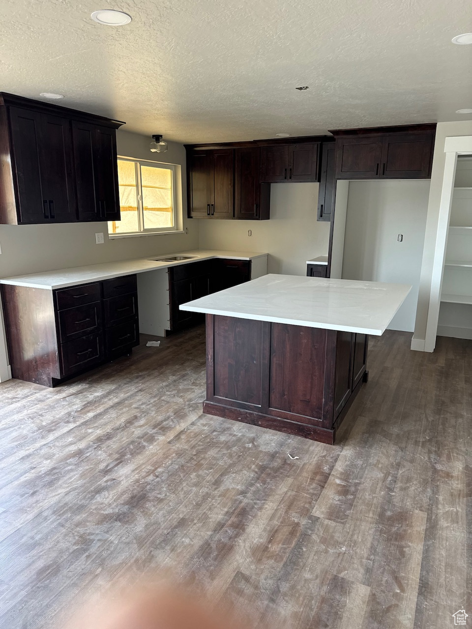 Kitchen featuring dark brown cabinetry, a textured ceiling, a center island, and wood finished floors