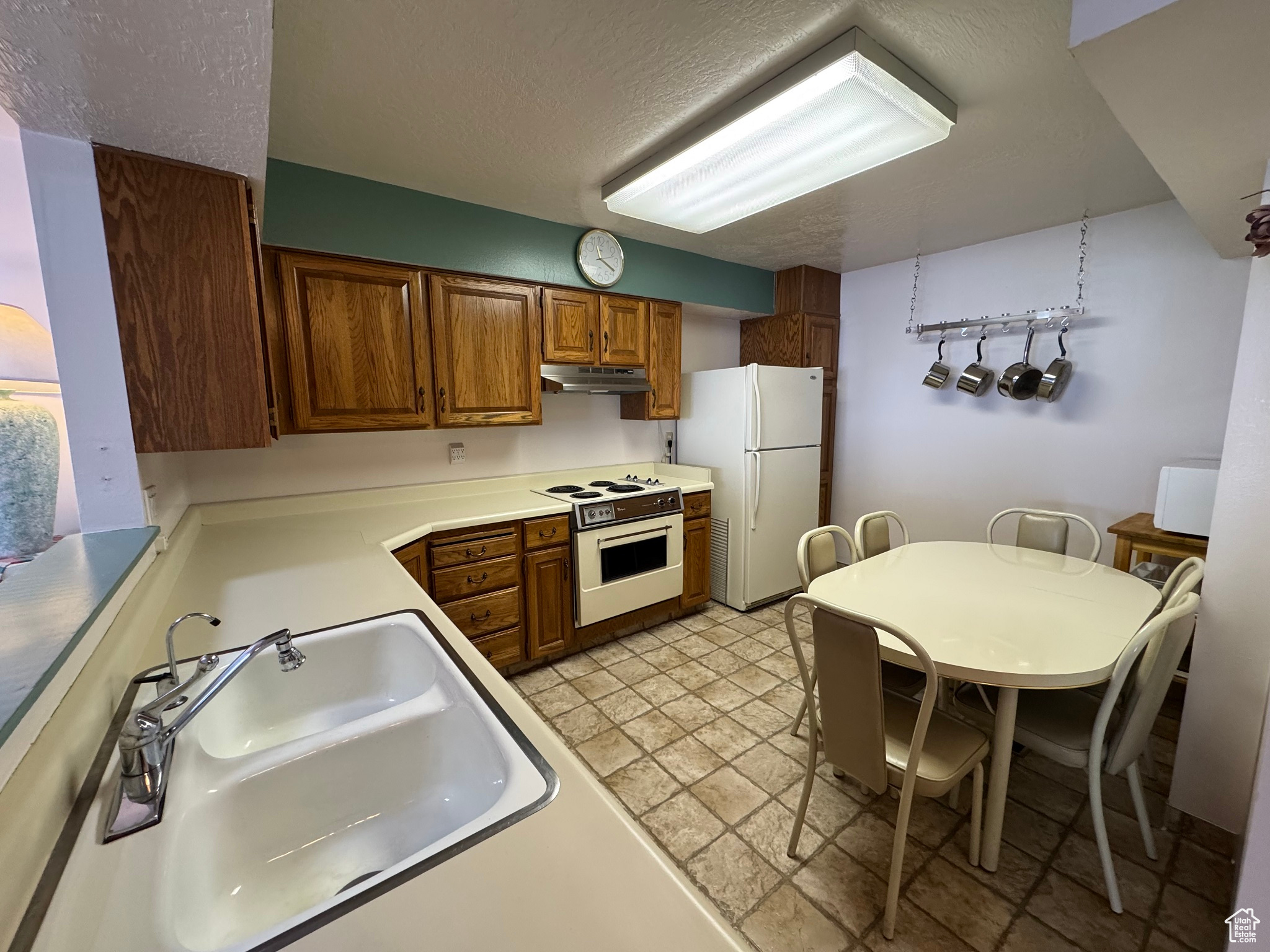 Kitchen with white appliances, a sink, under cabinet range hood, a textured ceiling, and brown cabinets