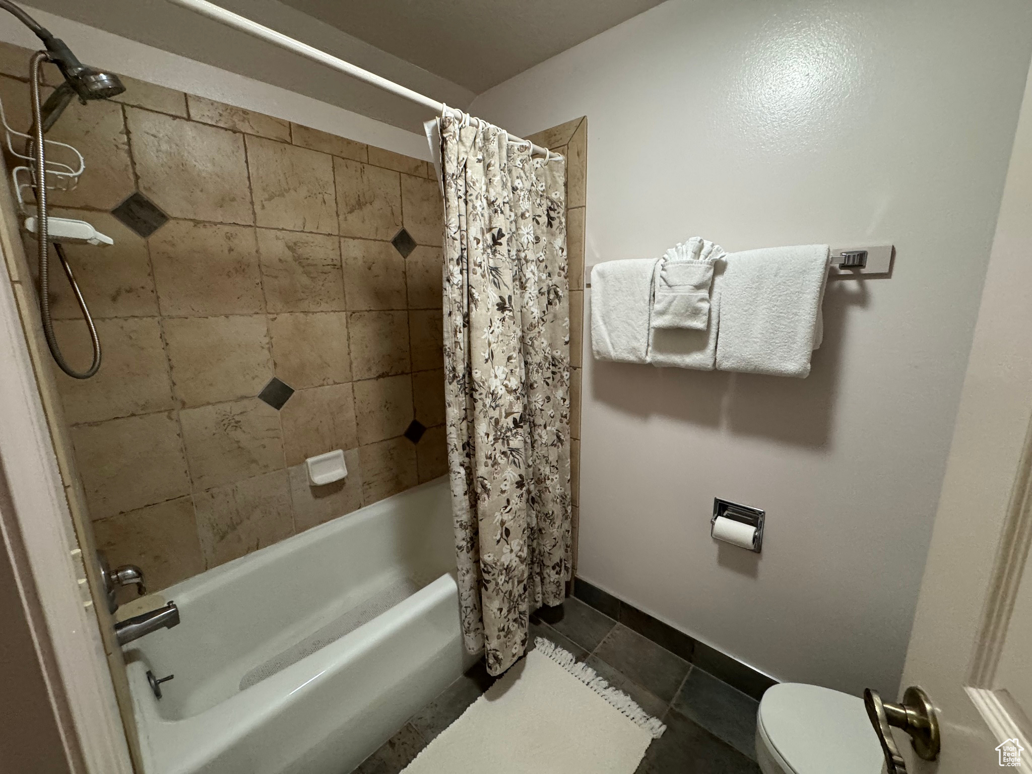 Bathroom featuring tile patterned floors, toilet, and shower / bathtub combination with curtain