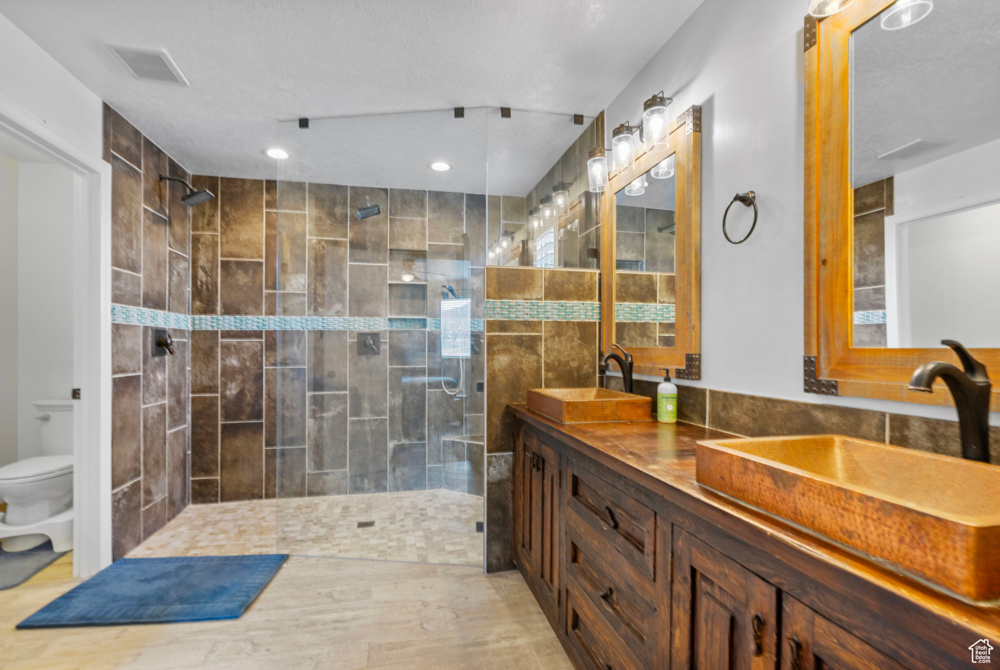 Bathroom featuring visible vents, toilet, walk in shower, and a sink