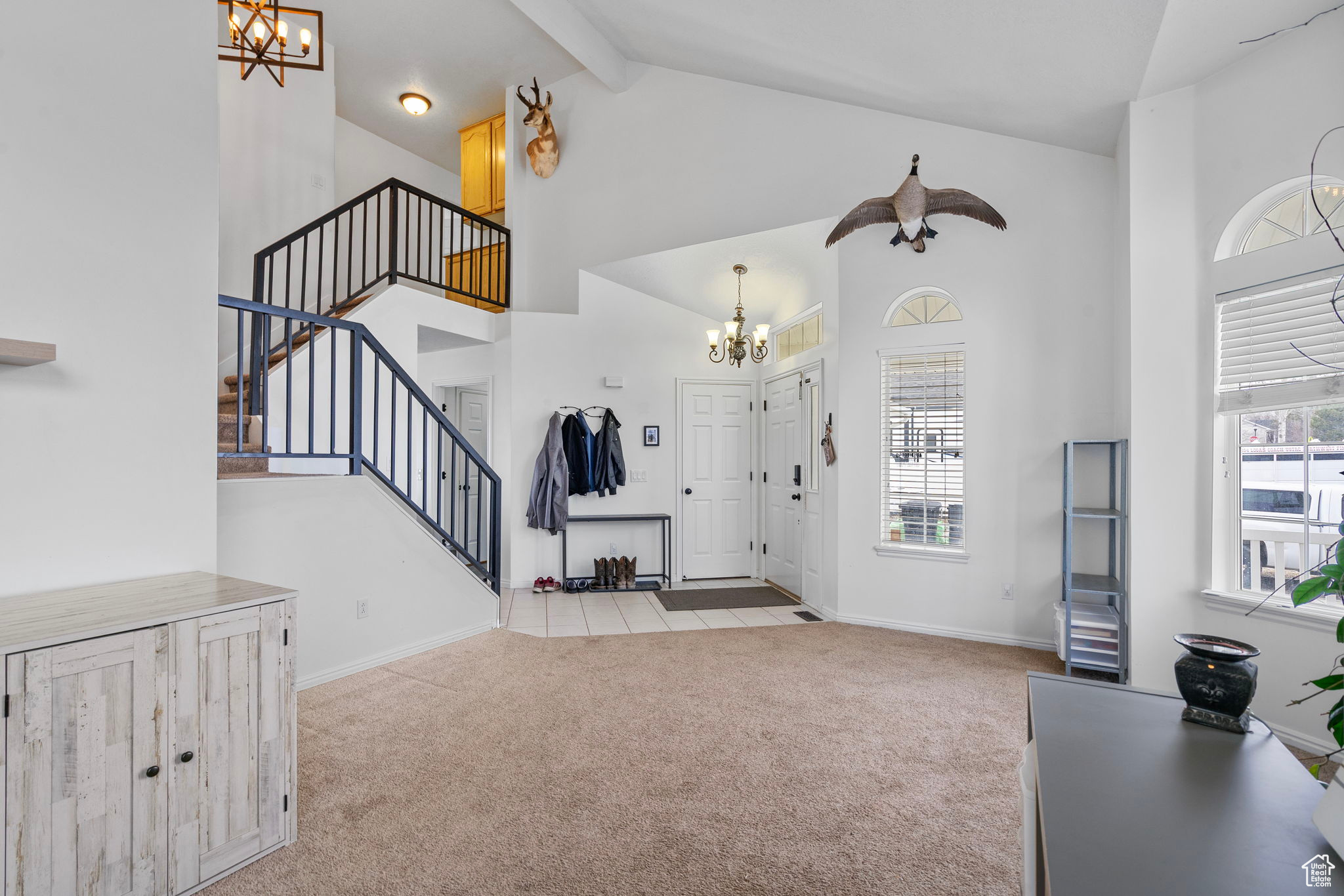 Carpeted foyer featuring stairs, an inviting chandelier, high vaulted ceiling, and beam ceiling