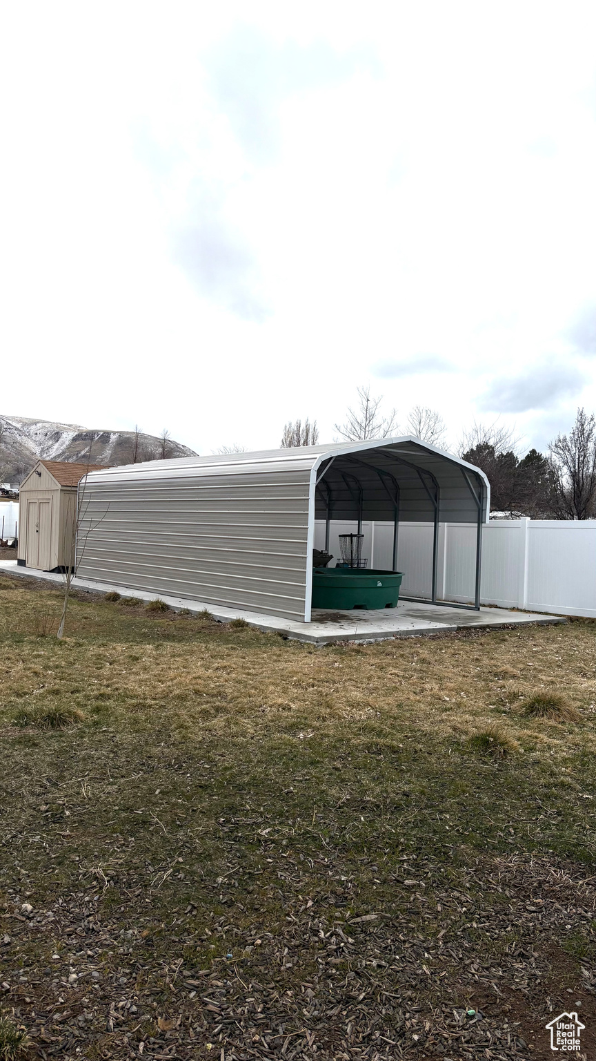 View of yard featuring a storage shed, a detached carport, fence, and an outbuilding