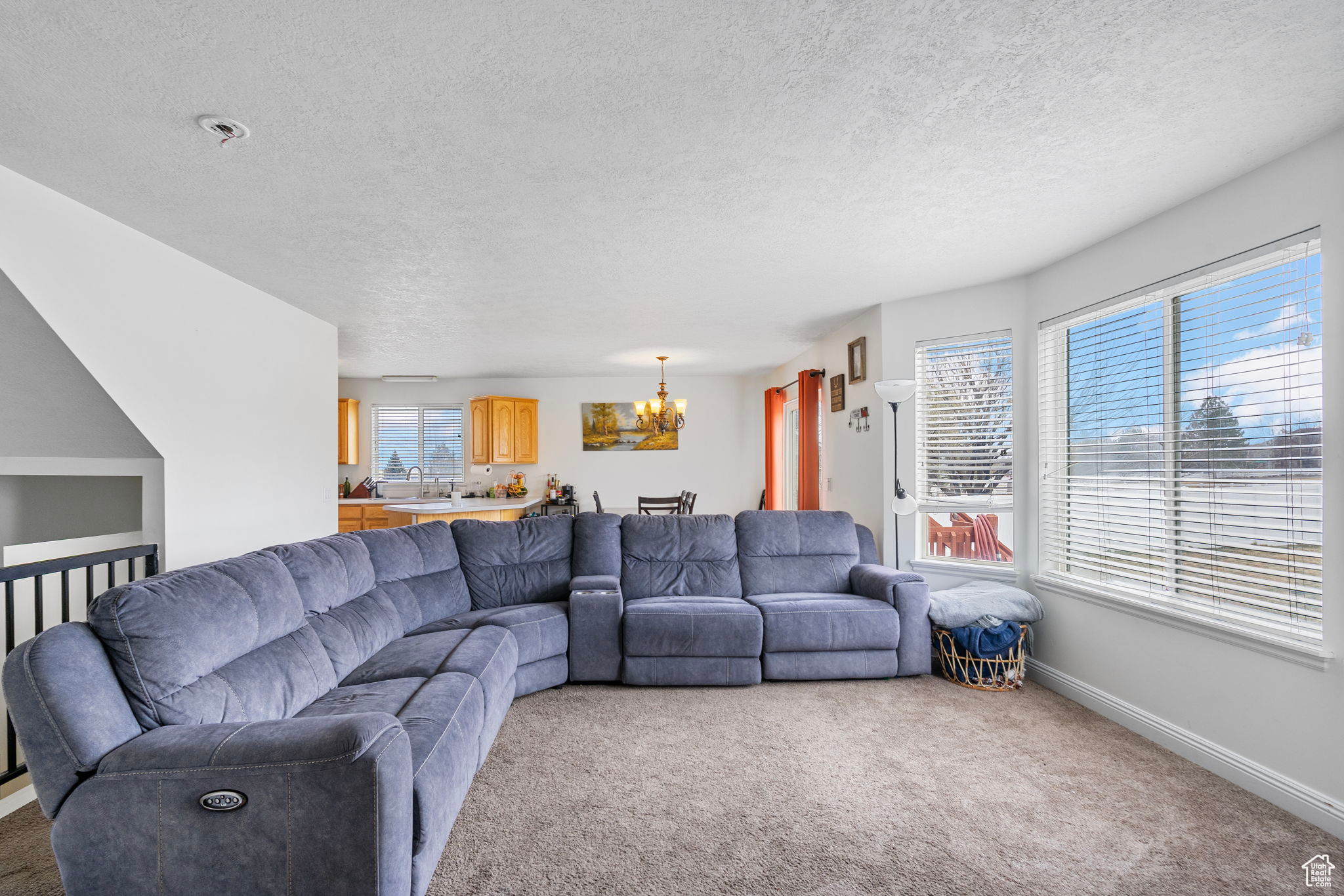 Living room with a notable chandelier, light colored carpet, baseboards, and a textured ceiling