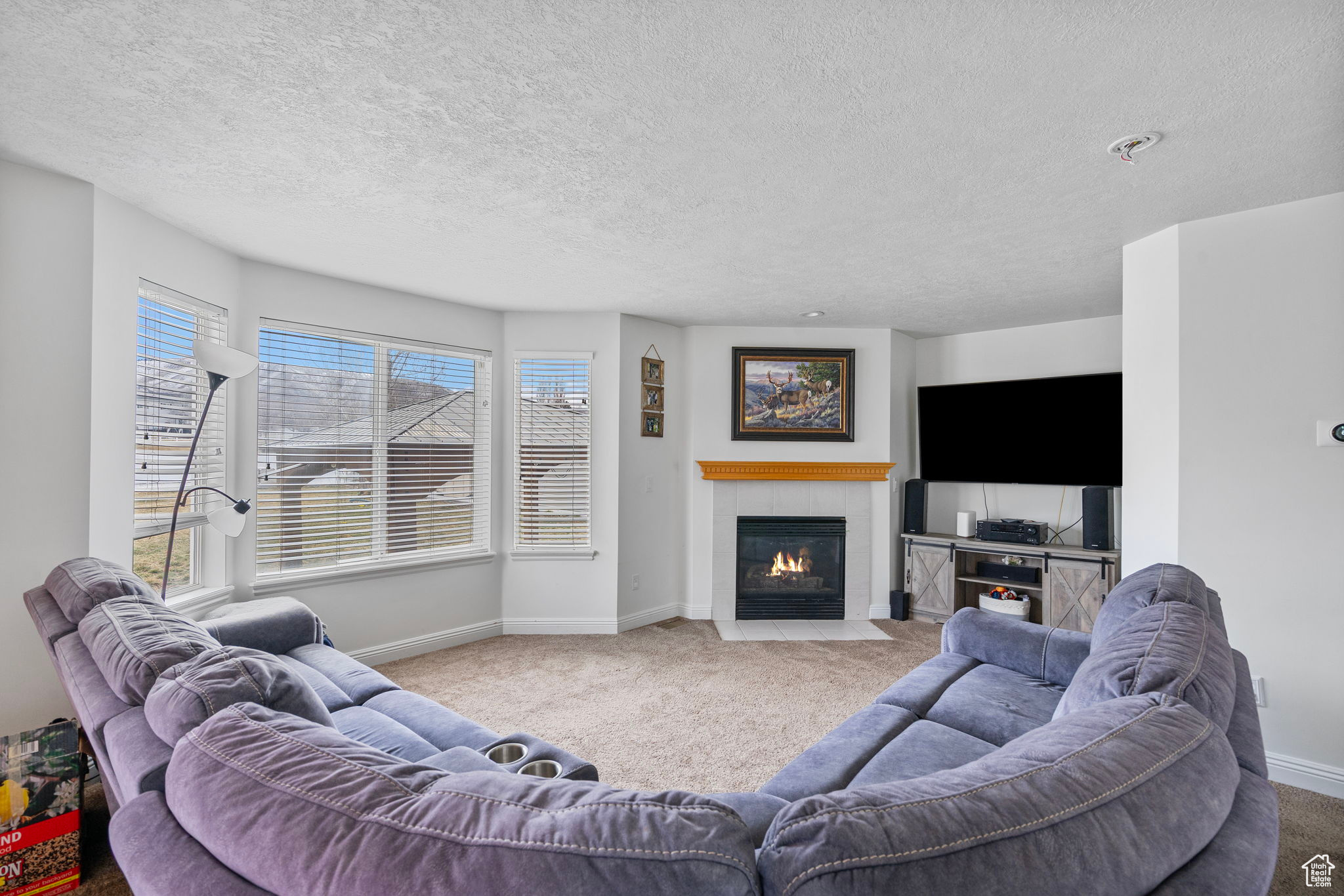 Carpeted living area featuring a textured ceiling, baseboards, and a tile fireplace