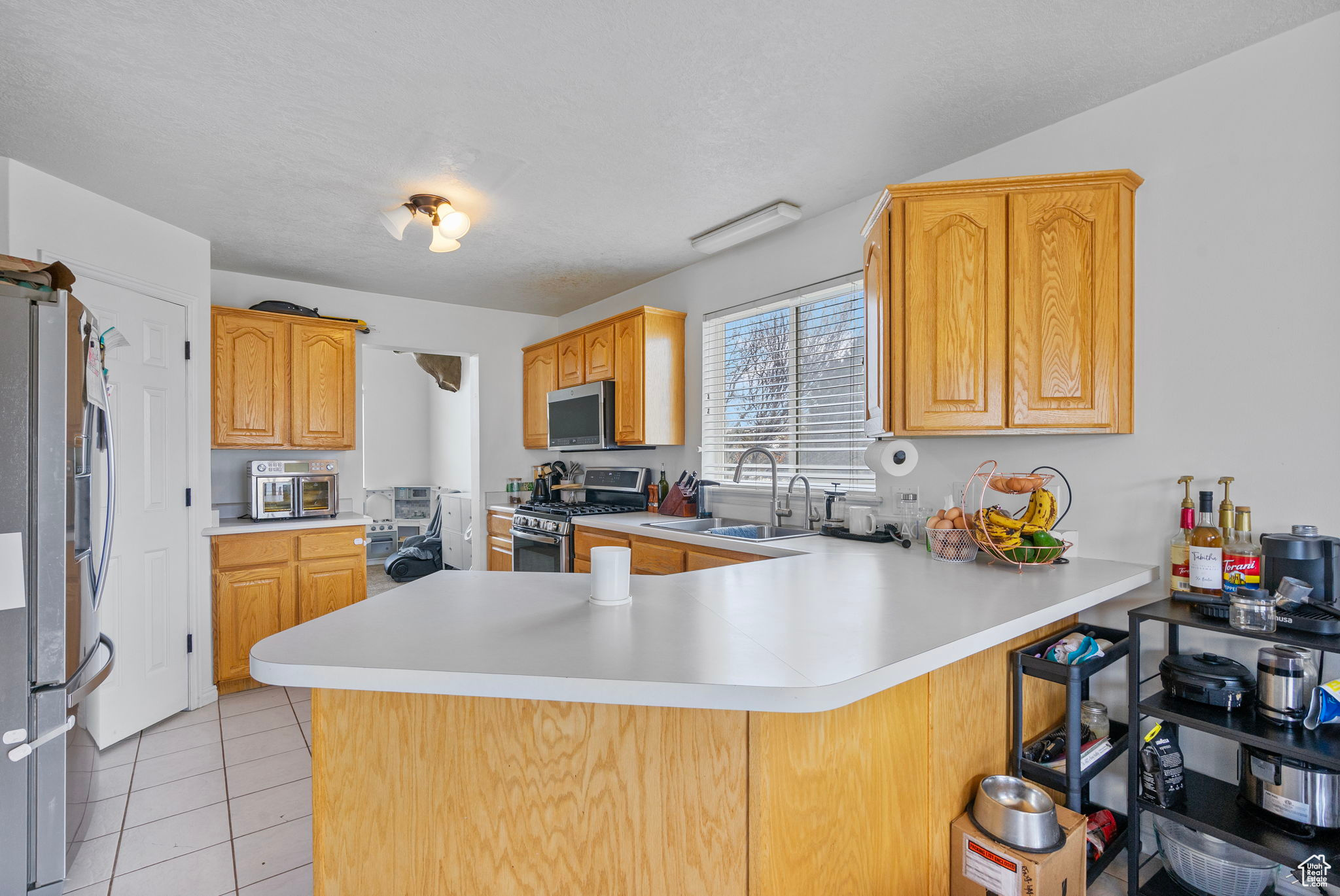 Kitchen with light tile patterned floors, a peninsula, a sink, light countertops, and appliances with stainless steel finishes