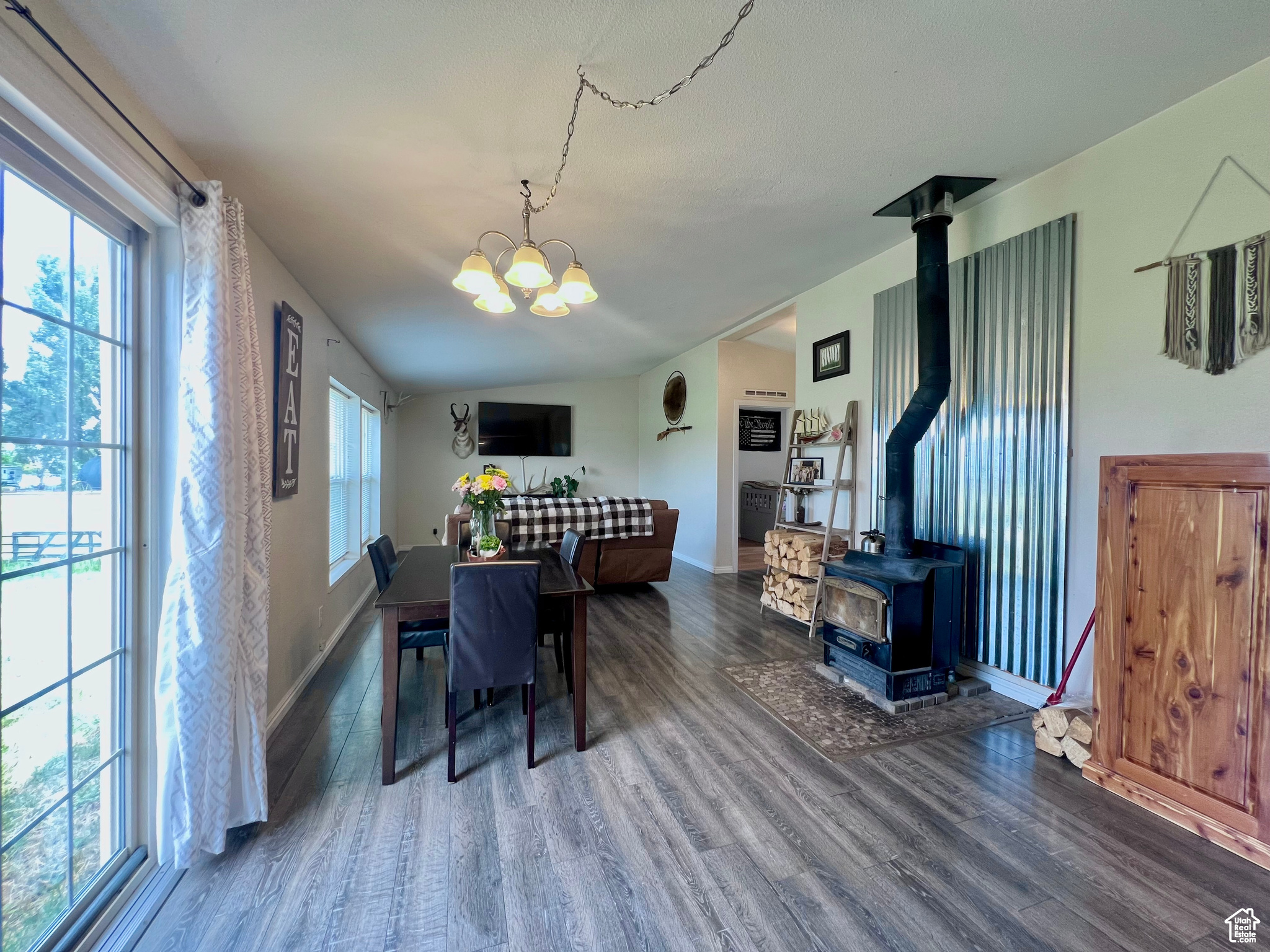 Dining area featuring baseboards, vaulted ceiling, a wood stove, wood finished floors, and a notable chandelier