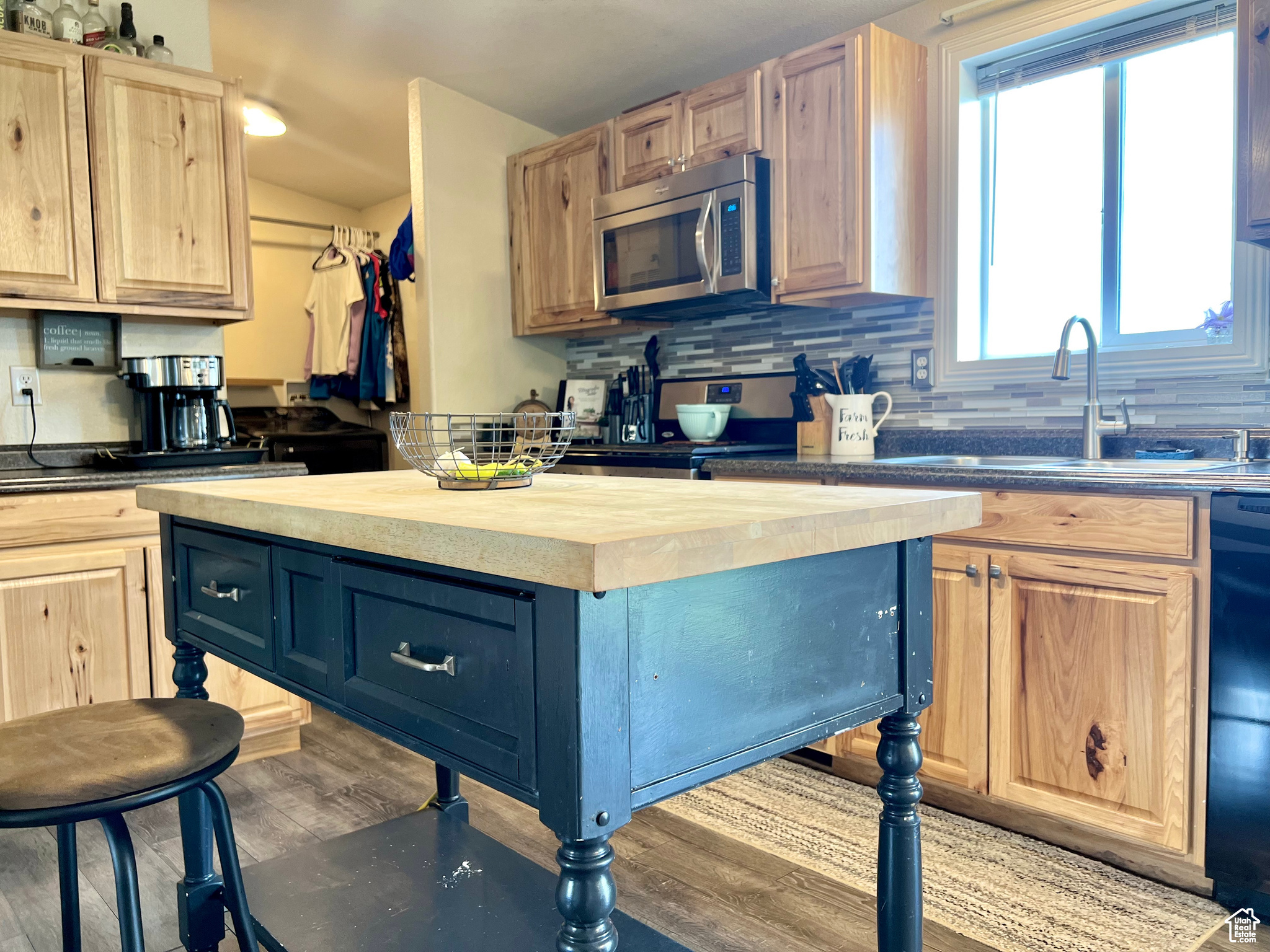 Kitchen featuring light brown cabinetry, butcher block countertops, light wood-style floors, appliances with stainless steel finishes, and tasteful backsplash