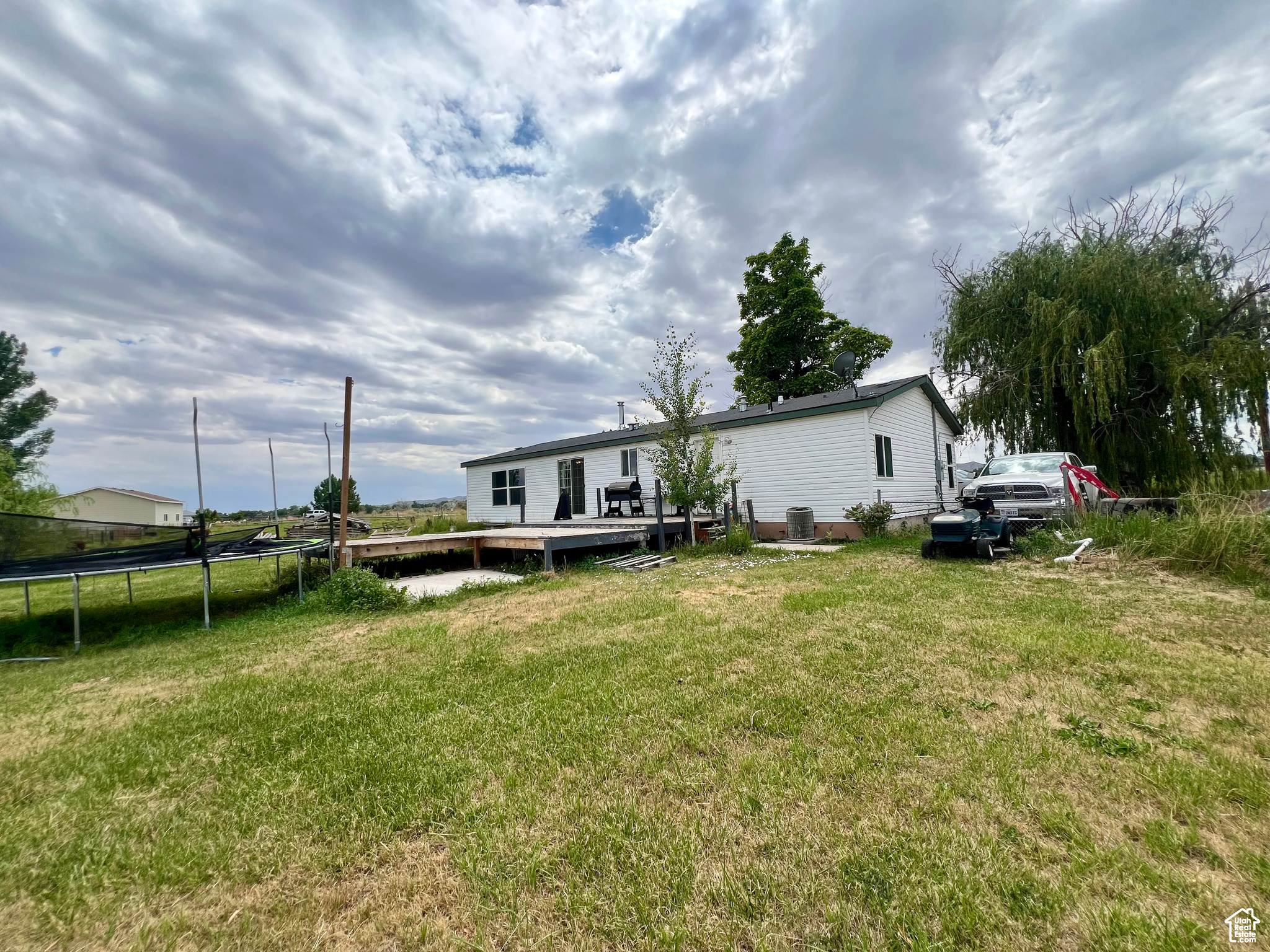 Back of house with a yard, a deck, central AC unit, and a trampoline