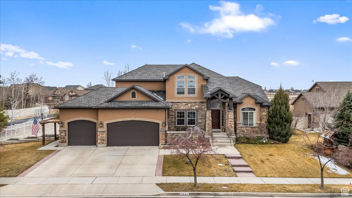 View of front facade with a garage, stone siding, driveway, and stucco siding