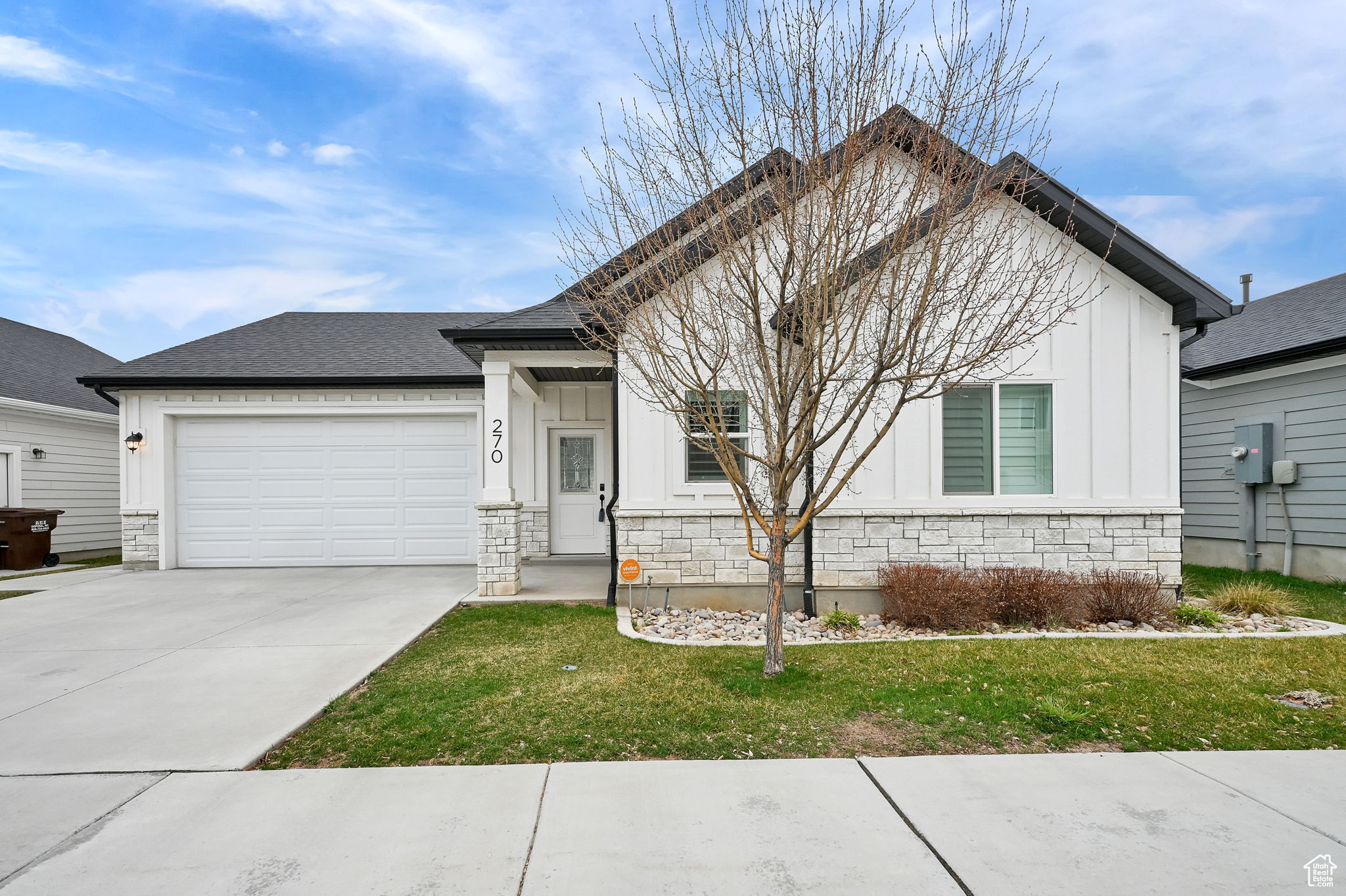Single story home featuring board and batten siding, an attached garage, stone siding, and driveway