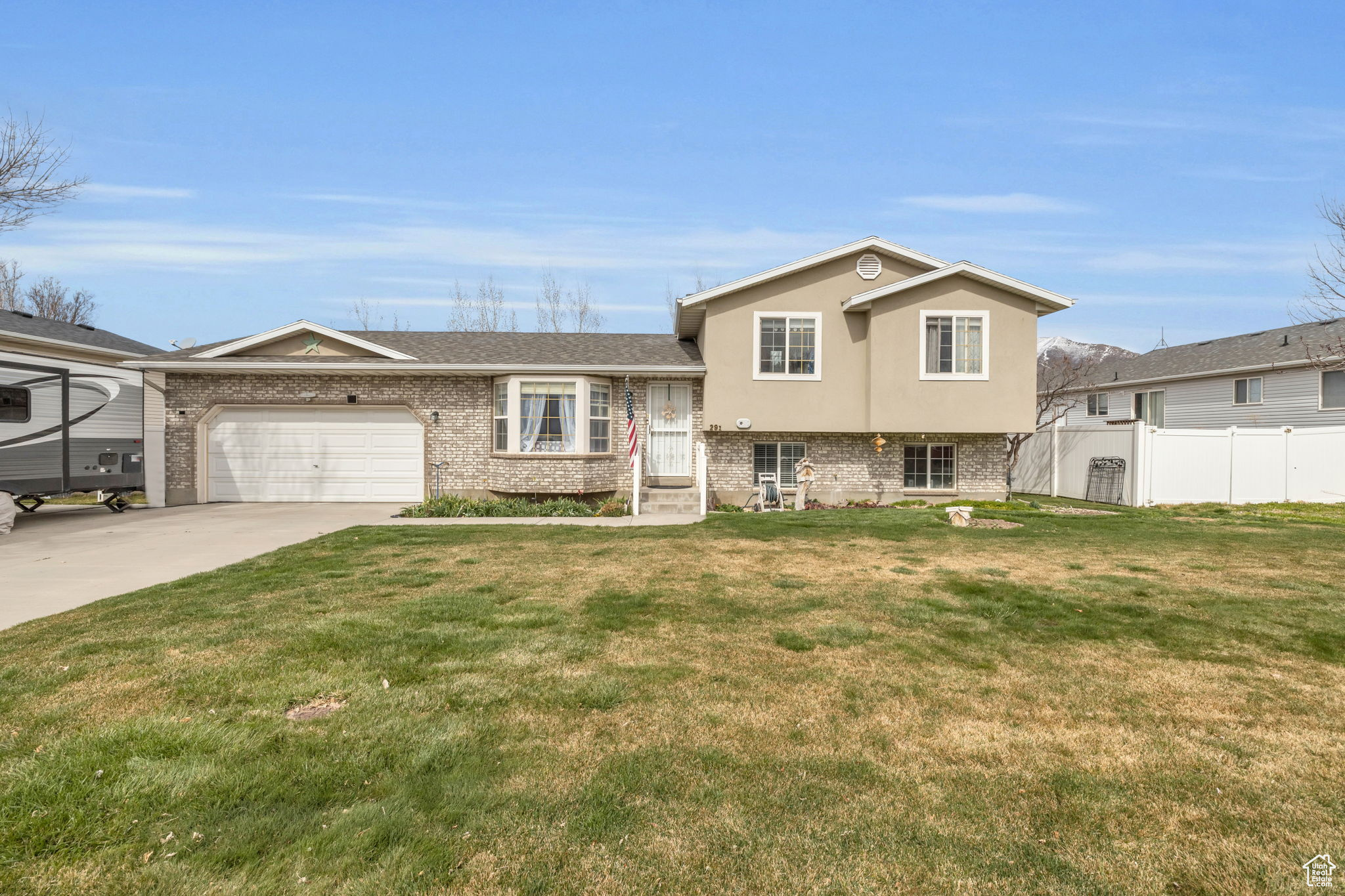 Split level home with a front yard, an attached garage, fence, and brick siding