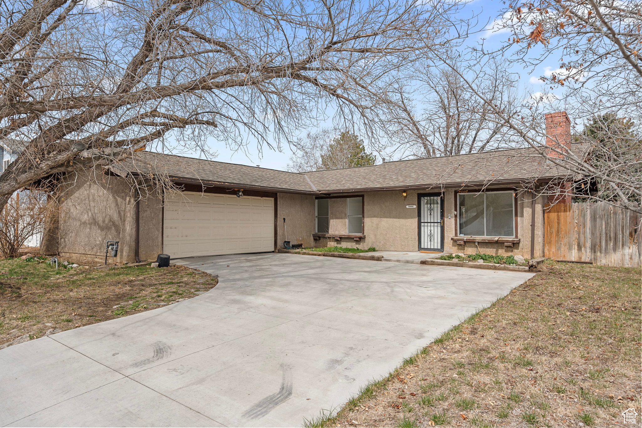 Single story home with a shingled roof, stucco siding, a chimney, a garage, and driveway