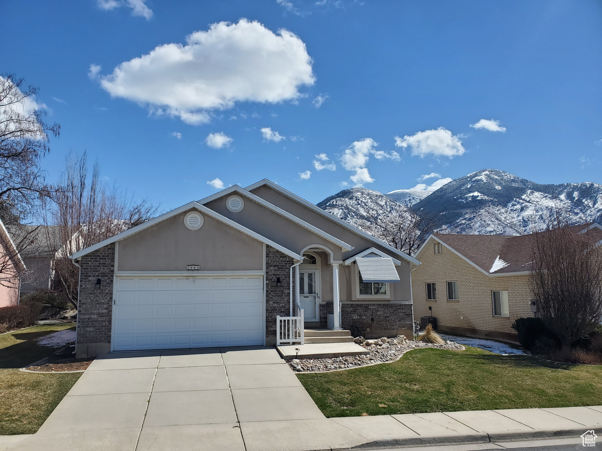Ranch-style house featuring a front lawn, a mountain view, concrete driveway, an attached garage, and brick siding