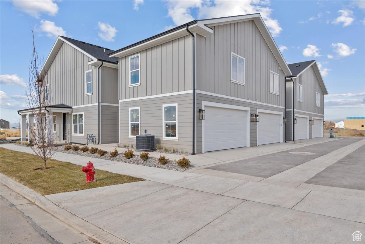 View of side of property with driveway, cooling unit, an attached garage, and board and batten siding