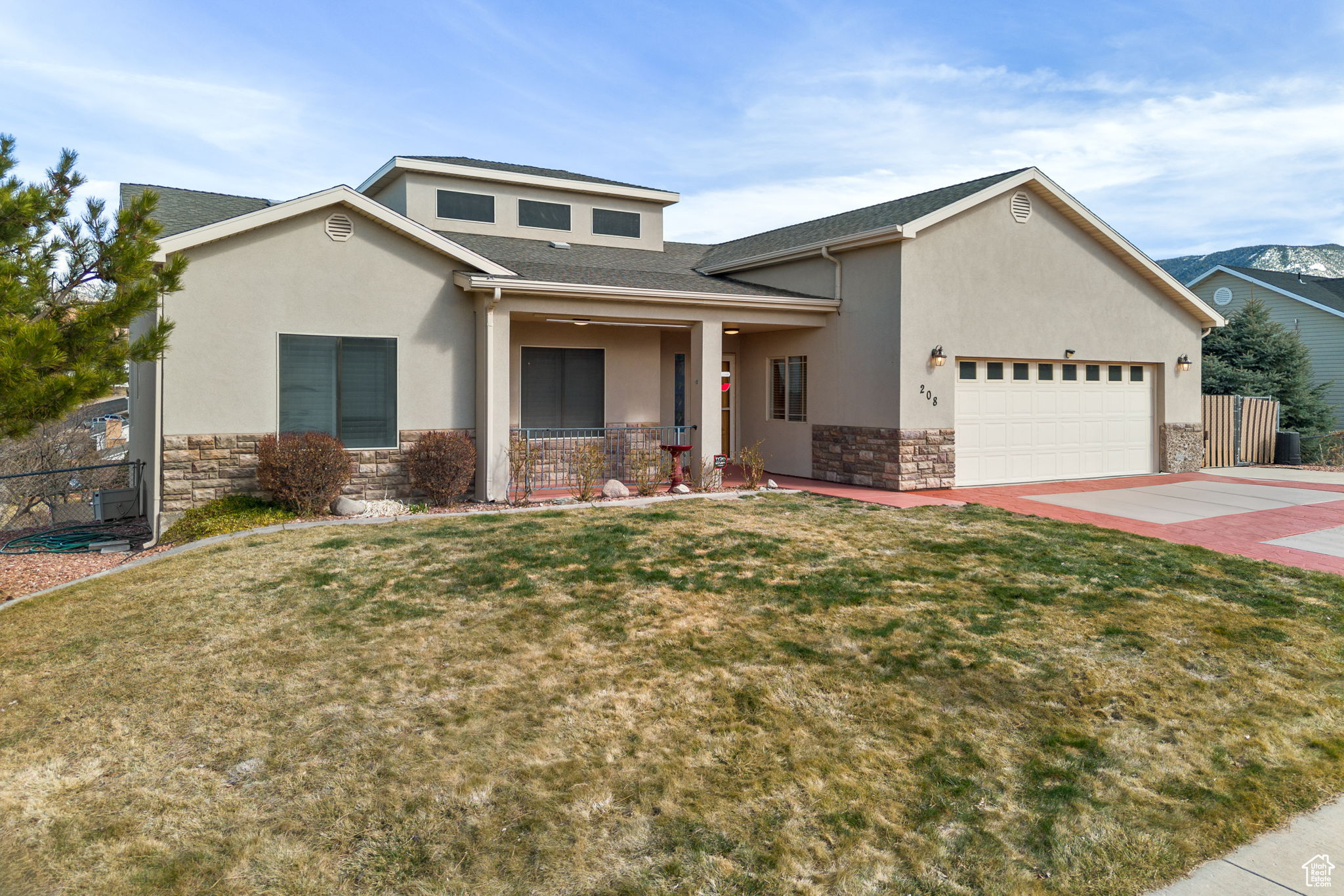 View of front of house featuring stone siding, concrete driveway, stucco siding, an attached garage, and a front lawn