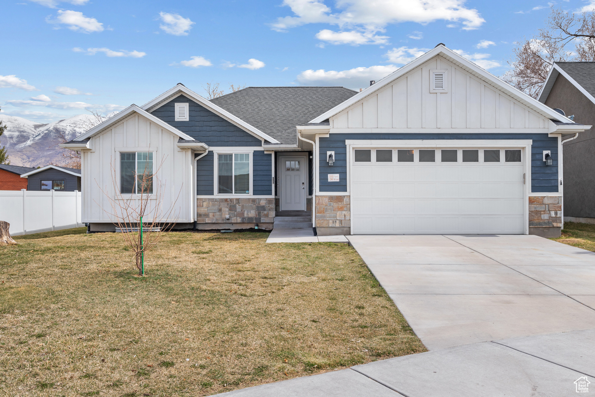 View of front of home featuring stone siding, fence, an attached garage, concrete driveway, and board and batten siding