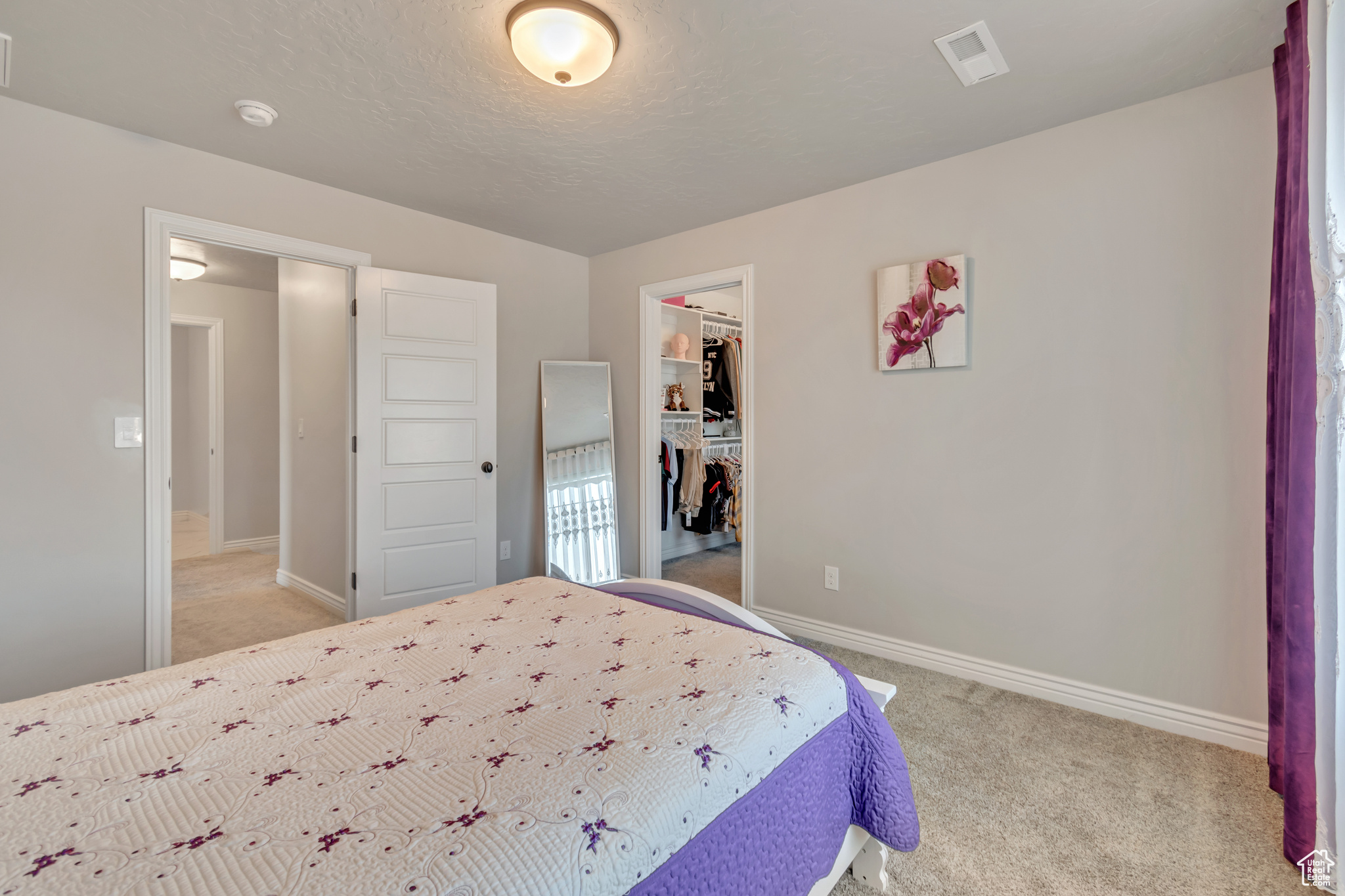 Bedroom featuring a closet, light carpet, a walk in closet, baseboards, and visible vents