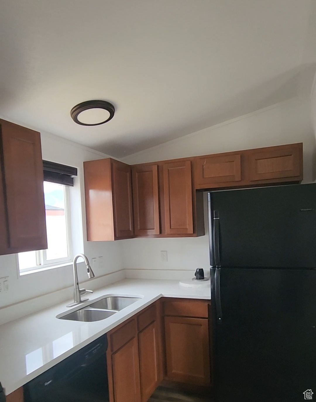 Kitchen with black appliances, light countertops, a sink, lofted ceiling, and brown cabinets