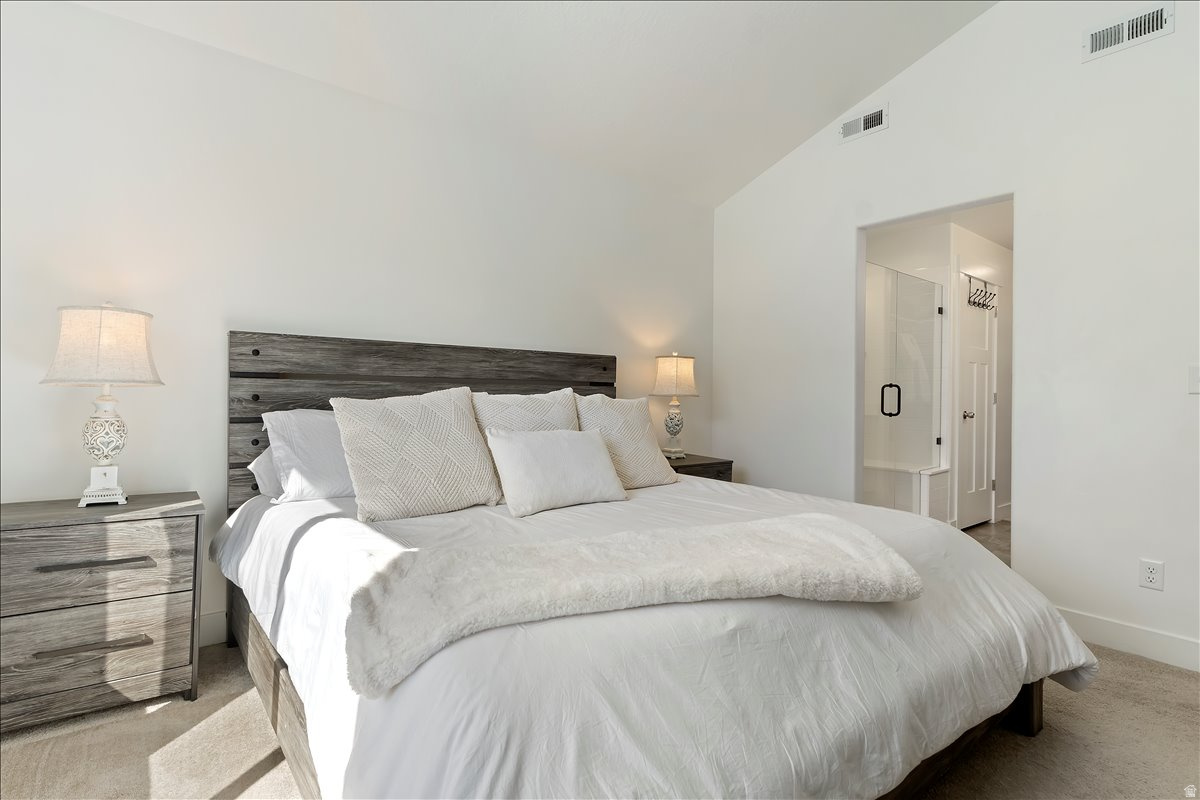 Bedroom featuring lofted ceiling, light carpet, and ensuite bathroom