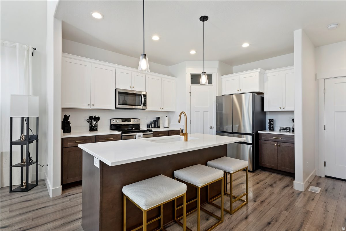 Kitchen with dual tone cabinets, stainless steel appliances, a kitchen bar, a center island with sink, and light wood-type flooring