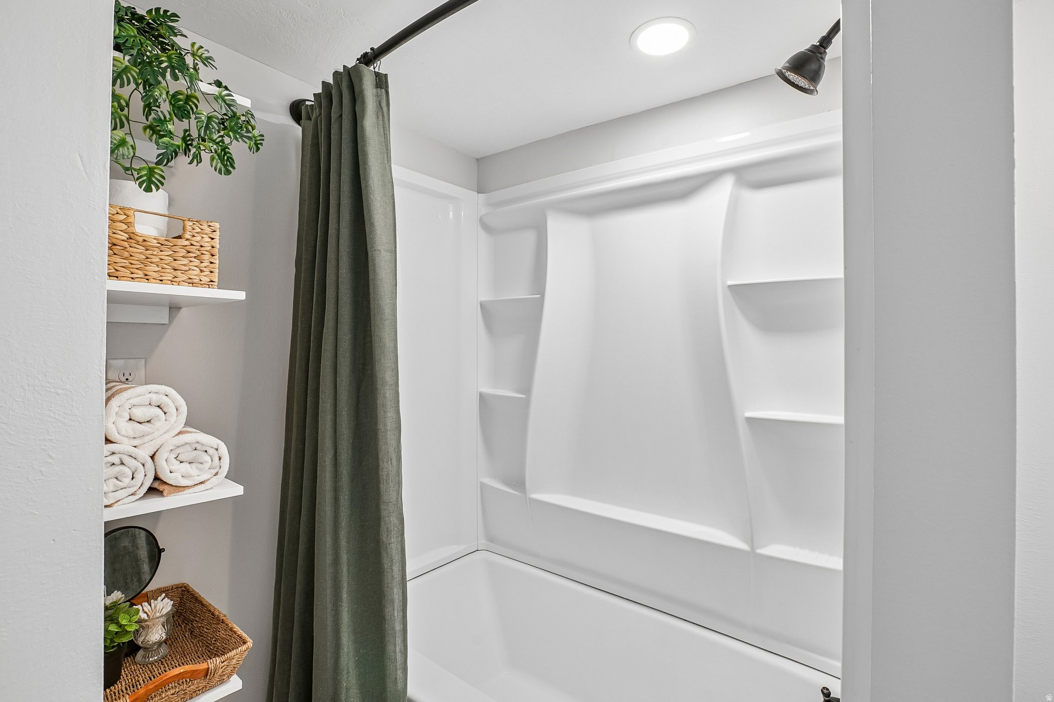 White bathtub and shower surround with integrated shelving, matte black shower head, recessed lighting, and built-in shelving