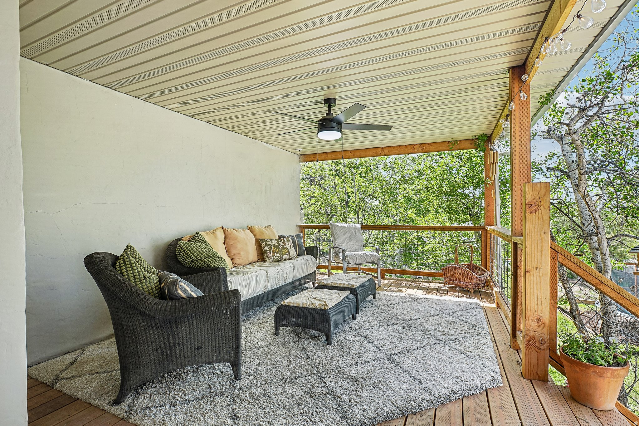 Covered outdoor deck with wood-finish flooring, featuring a ceiling fan with integrated lighting and a wood railing with cable infill