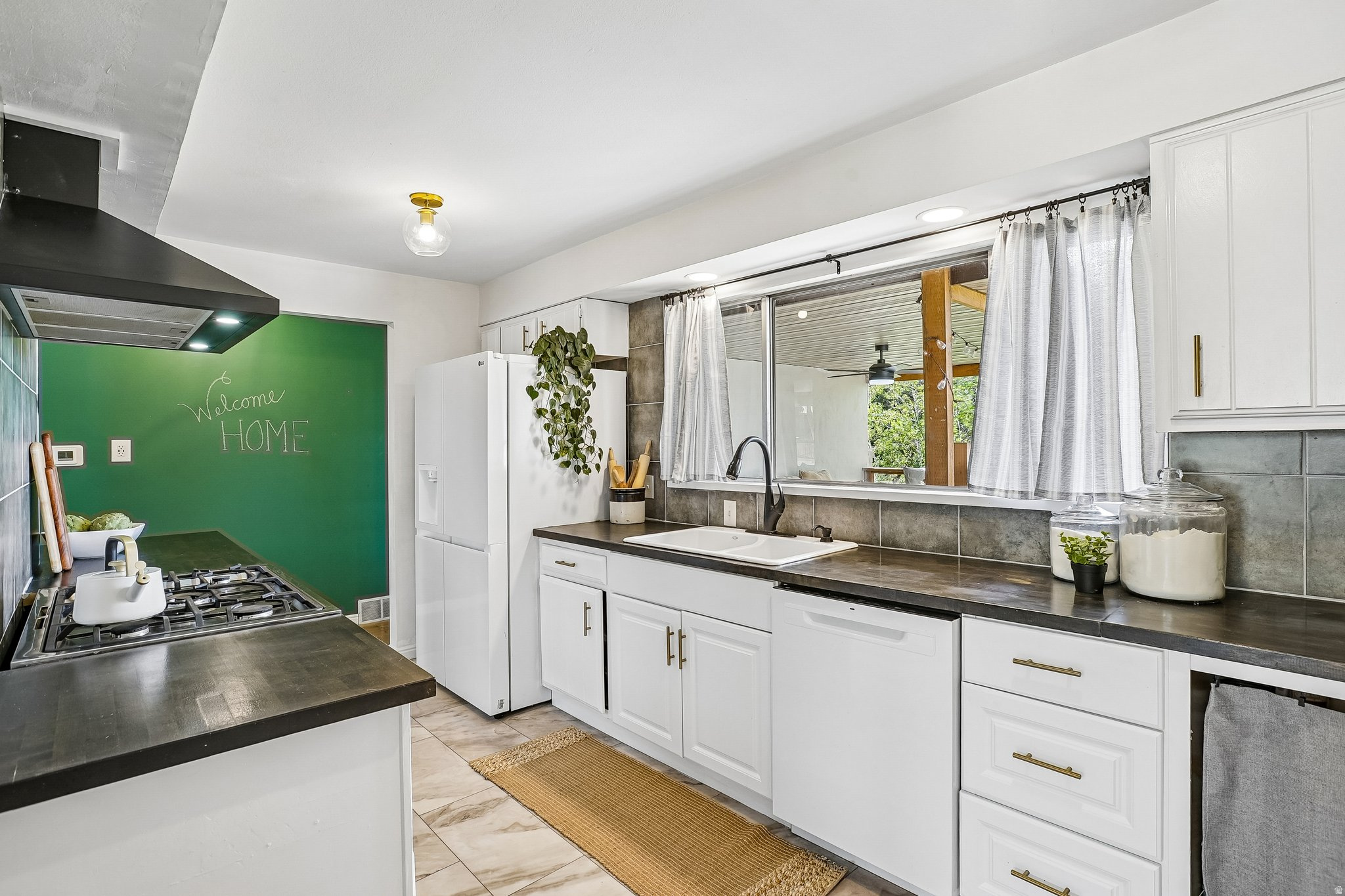 Spacious kitchen featuring white cabinetry with gold-toned hardware, dark countertops, and a tiled backsplash
