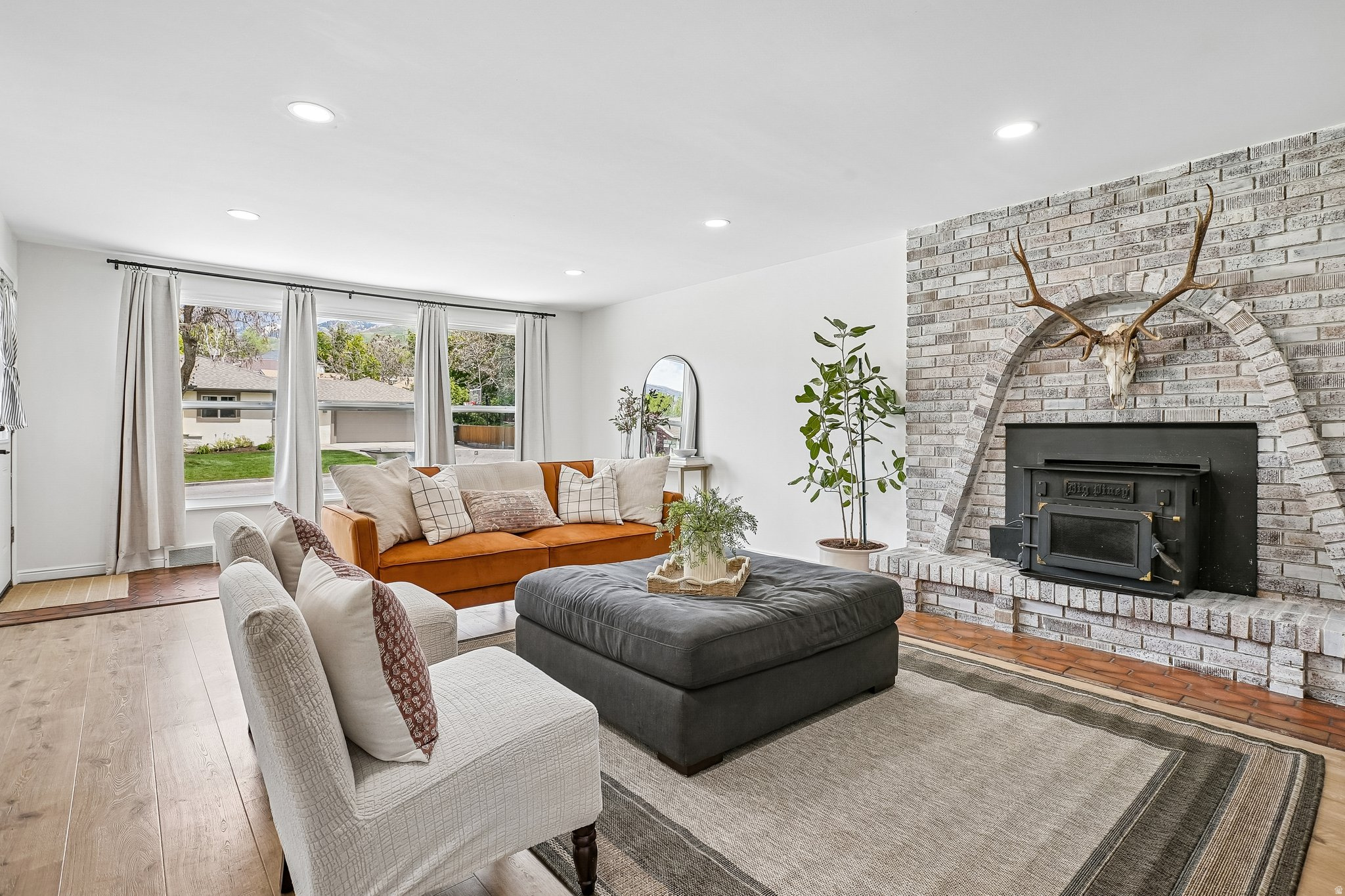 Living area featuring light wood-finish flooring, recessed lighting, and a brick fireplace with a wood-burning insert