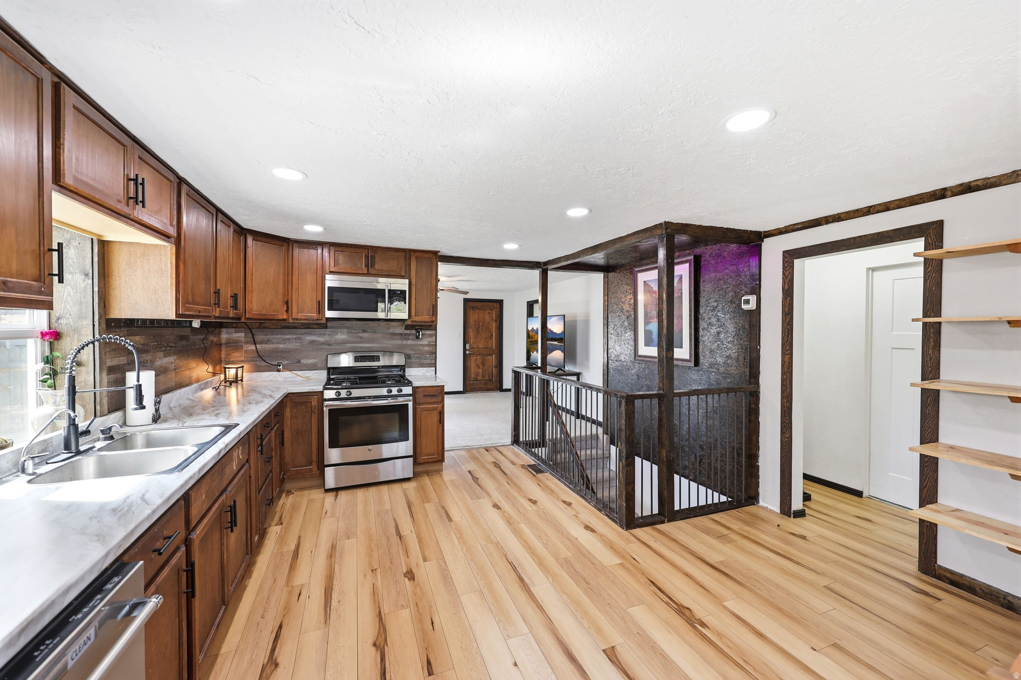 Kitchen featuring stainless steel appliances, light wood finished floors, recessed lighting, tasteful backsplash, and light stone counters