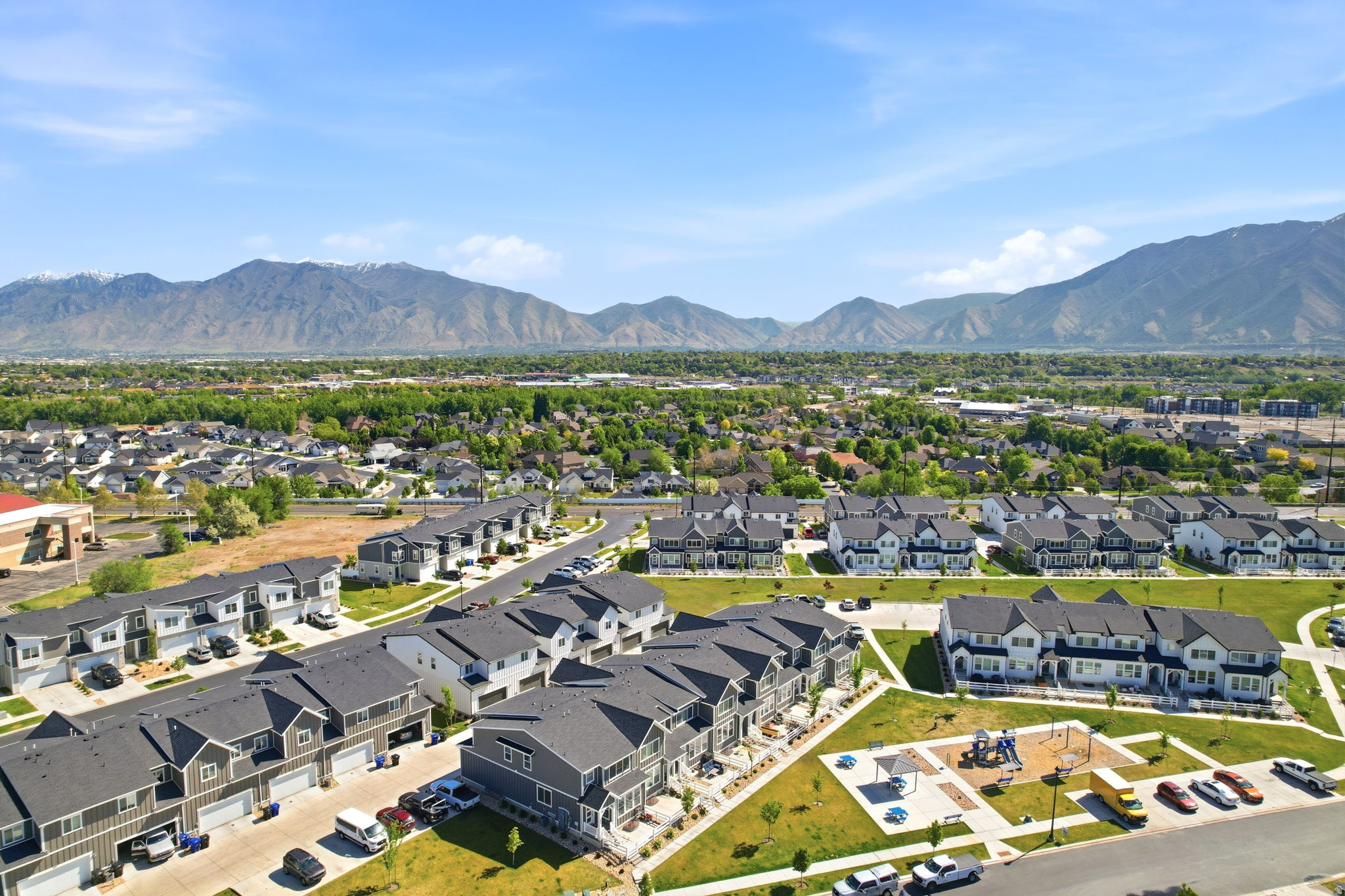 Aerial perspective showcasing a community of multi-level townhomes with dark roofs and light-colored siding, complemented by distant mountain ranges