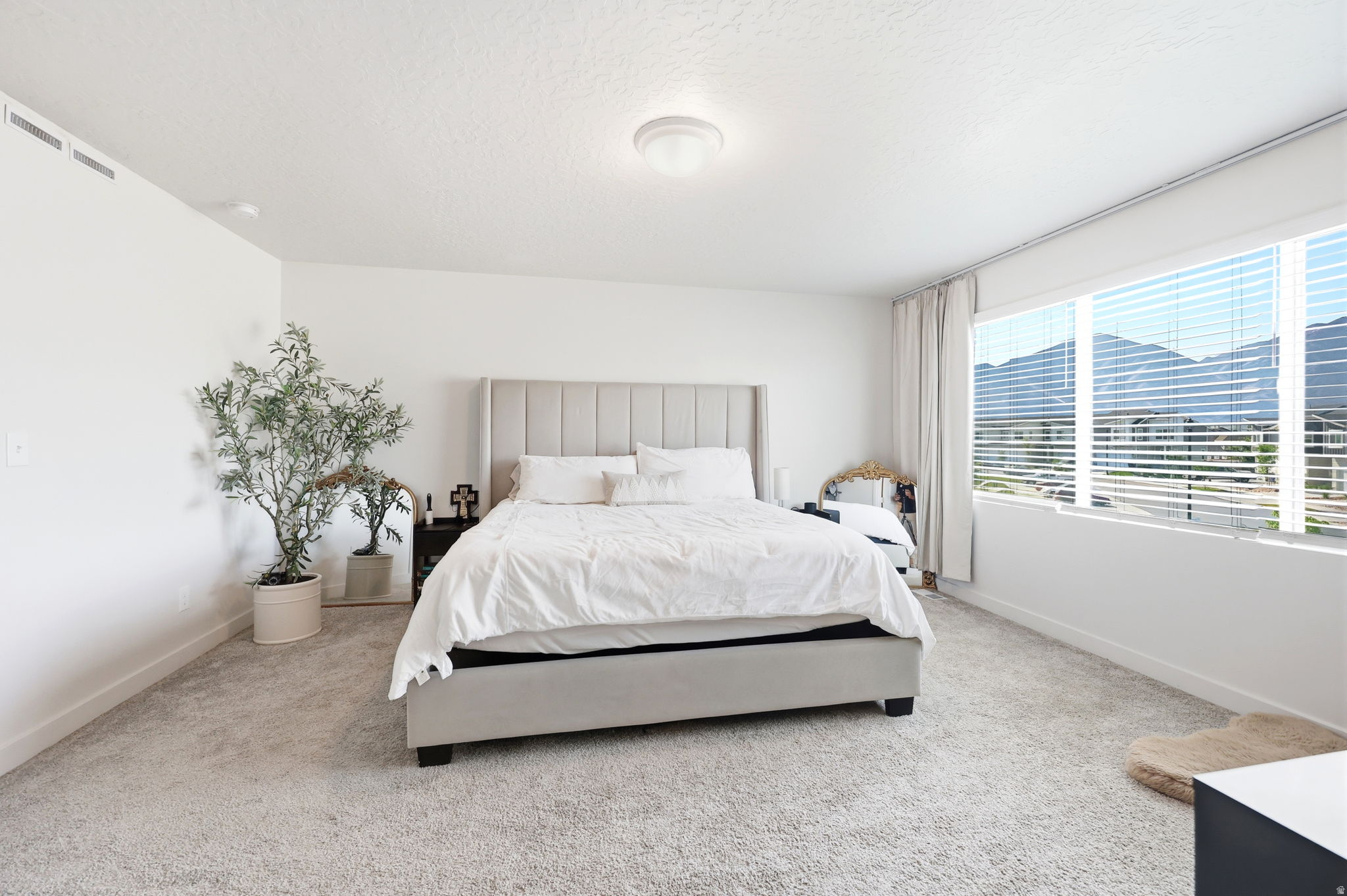 Bedroom featuring expansive windows with mountain scenery, light-colored carpet flooring, a contemporary ceiling light fixture, and white walls