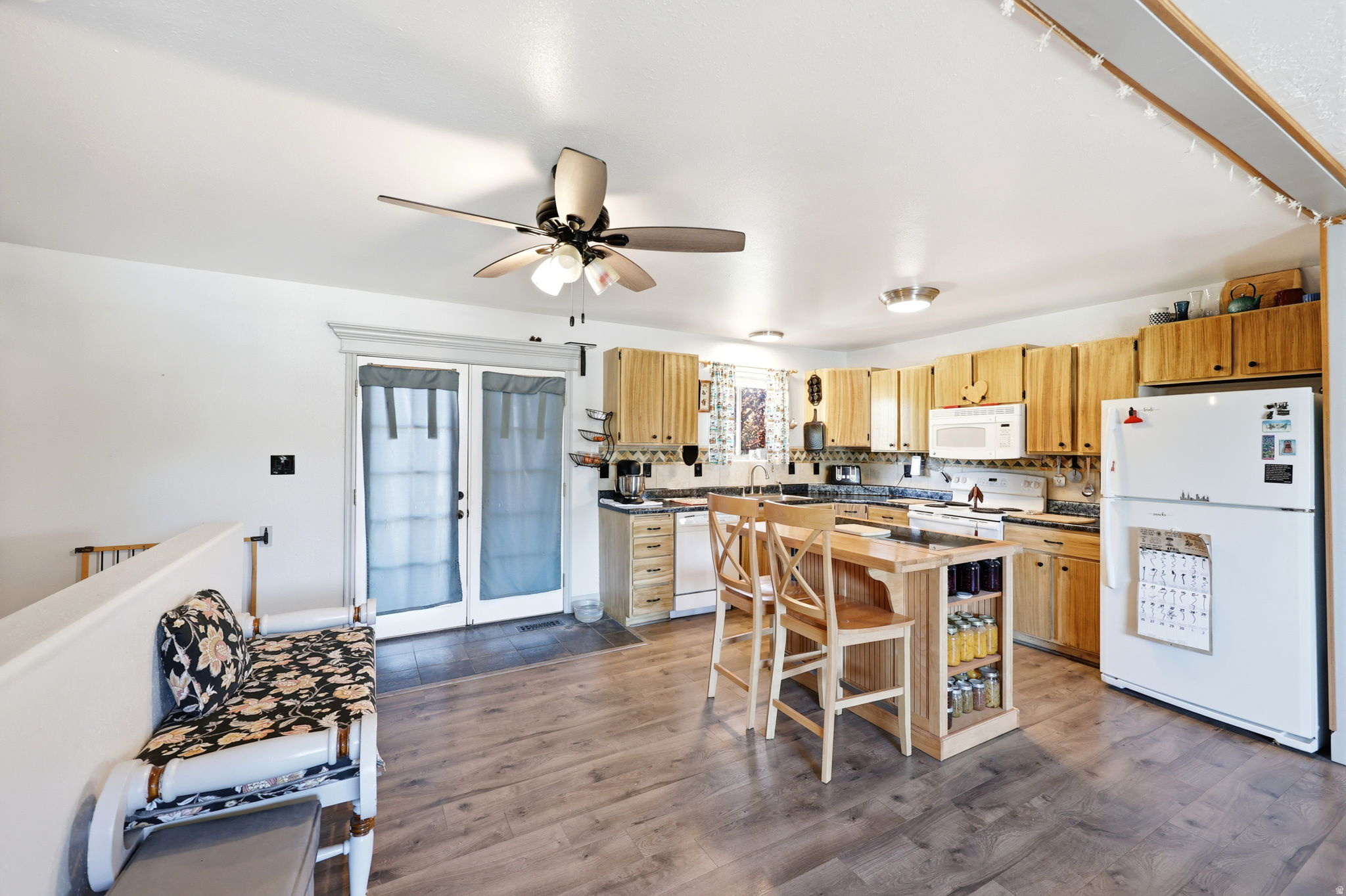 Spacious kitchen featuring wood-finish flooring, light wood cabinetry, white appliances, and a central island with integrated shelving