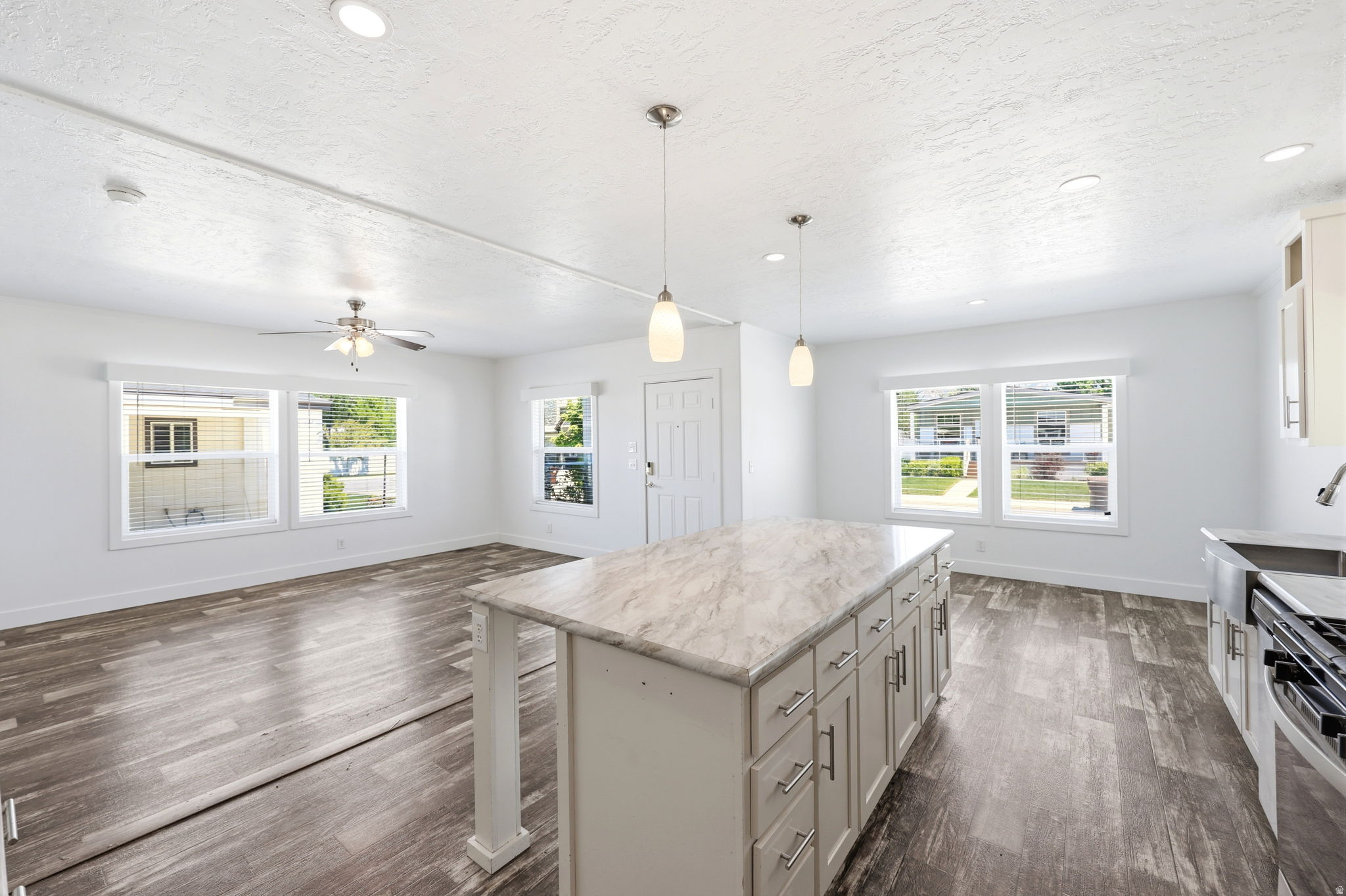 Open-concept interior featuring an expansive kitchen island with a light-toned countertop, pendant lighting, wood-finish flooring, recessed lighting, and white walls