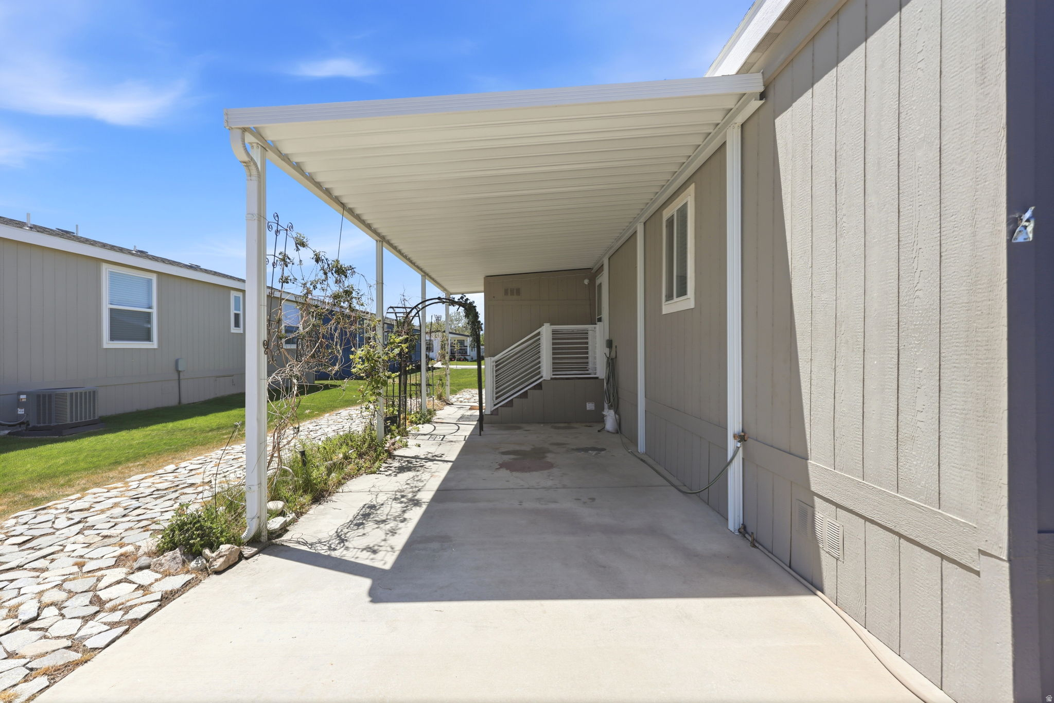 Covered concrete patio with white metal railings and vertical siding