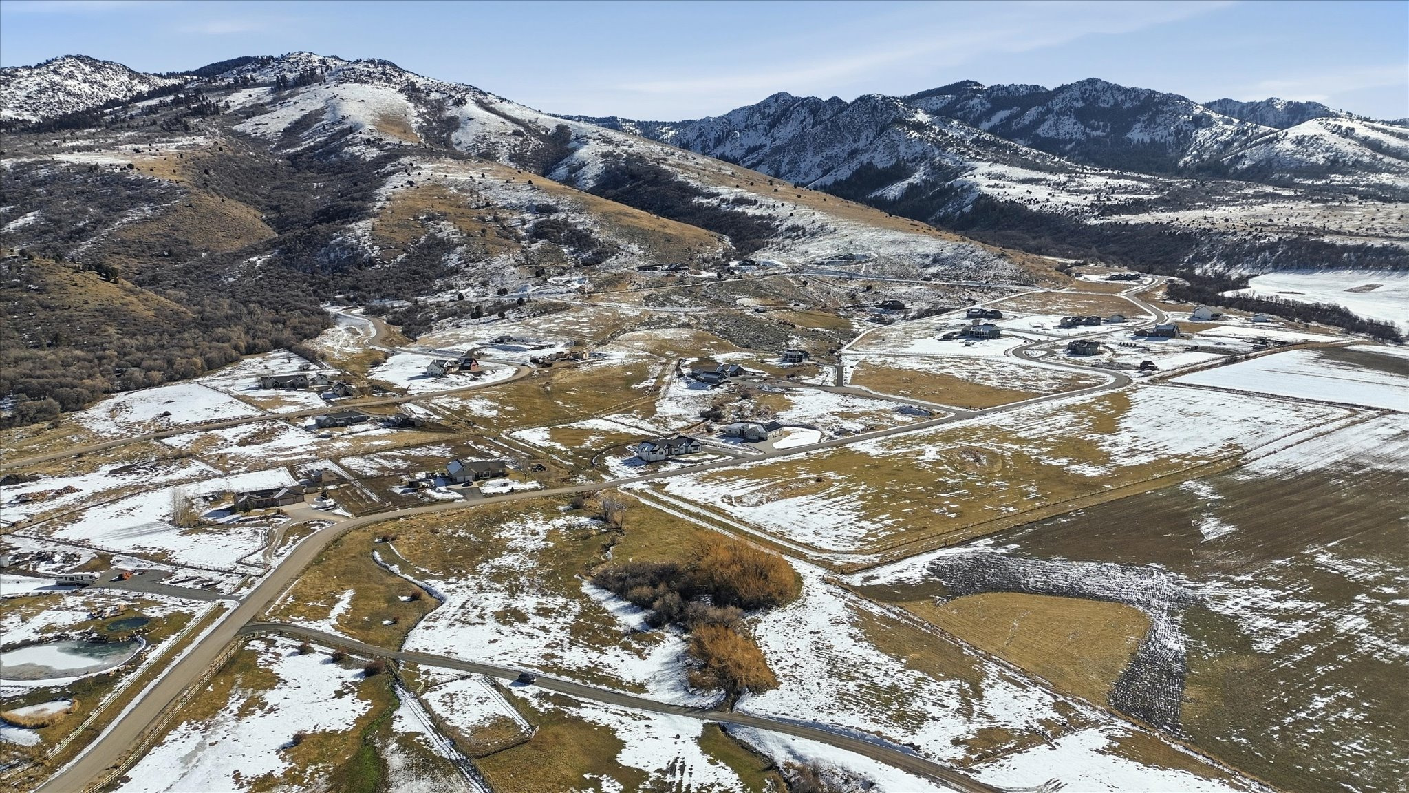 Expansive mountain landscape featuring snow-dusted terrain, scattered residential properties, natural waterways, and agricultural fields