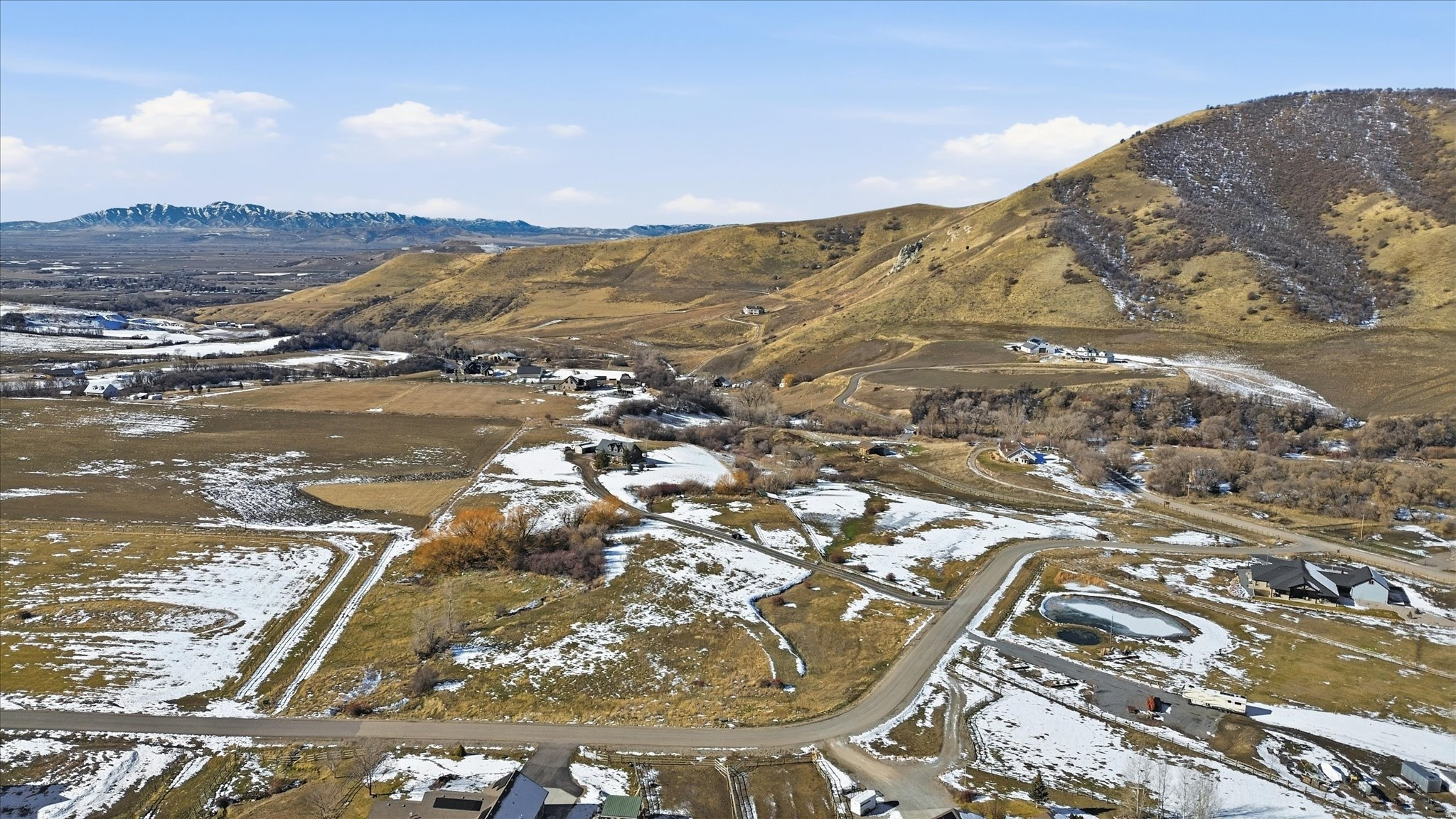 Expansive rural landscape featuring rolling hills, distant mountains, and scattered residential properties