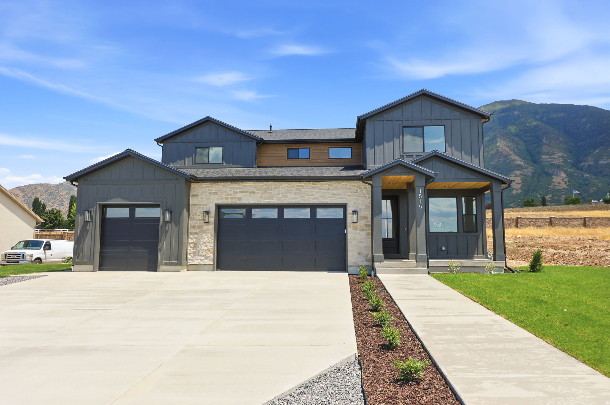 Contemporary multi-level residence featuring board and batten siding, stone veneer accents, a covered front porch, a three-car garage, and a concrete driveway