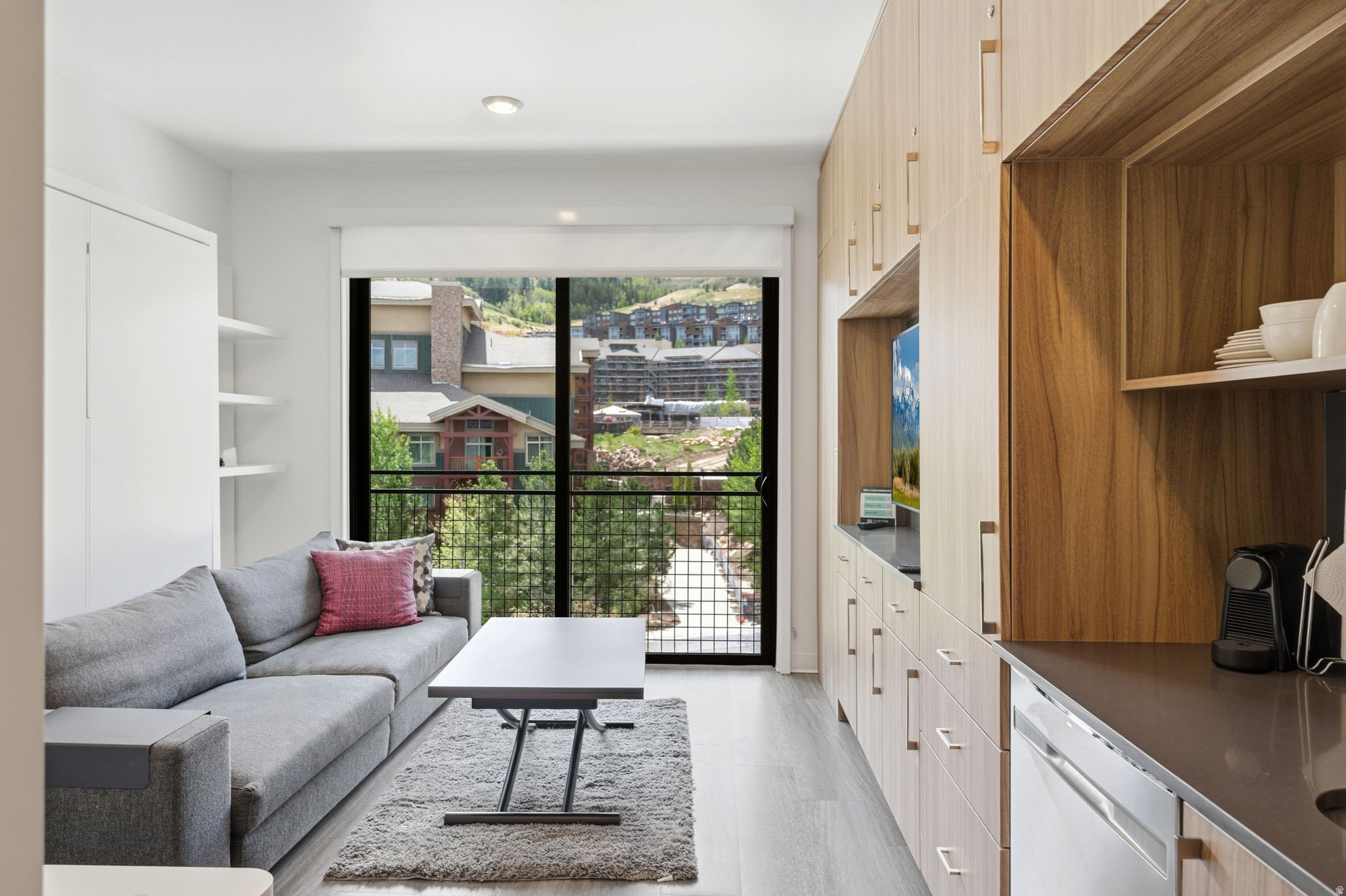 Open-concept living area featuring wood-finish flooring, a full wall of integrated cabinetry with open shelving, and a built-in dishwasher