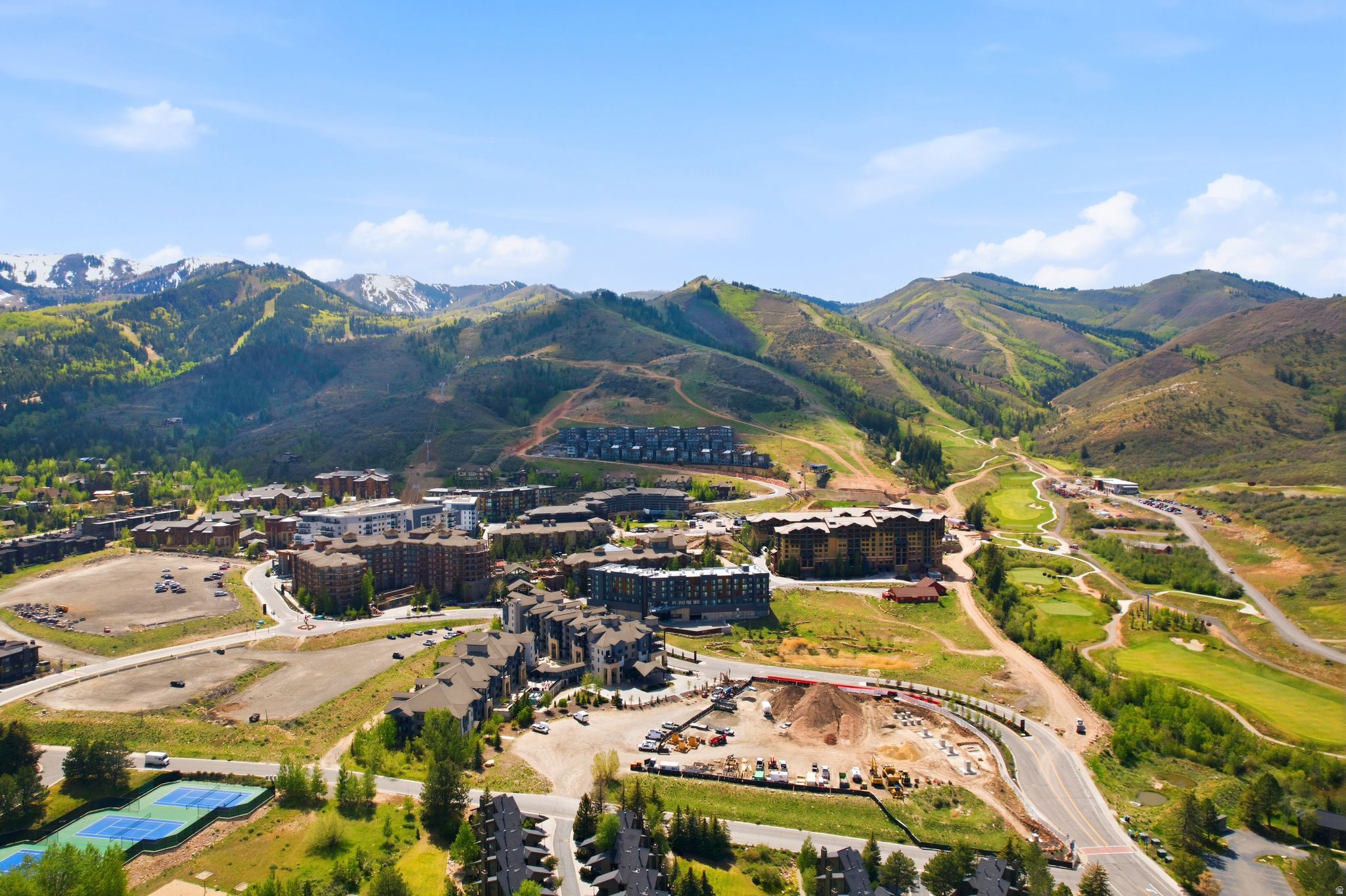 Aerial perspective of a mountain community featuring multiple residential structures, green hillsides, and snow-capped peaks in the distance