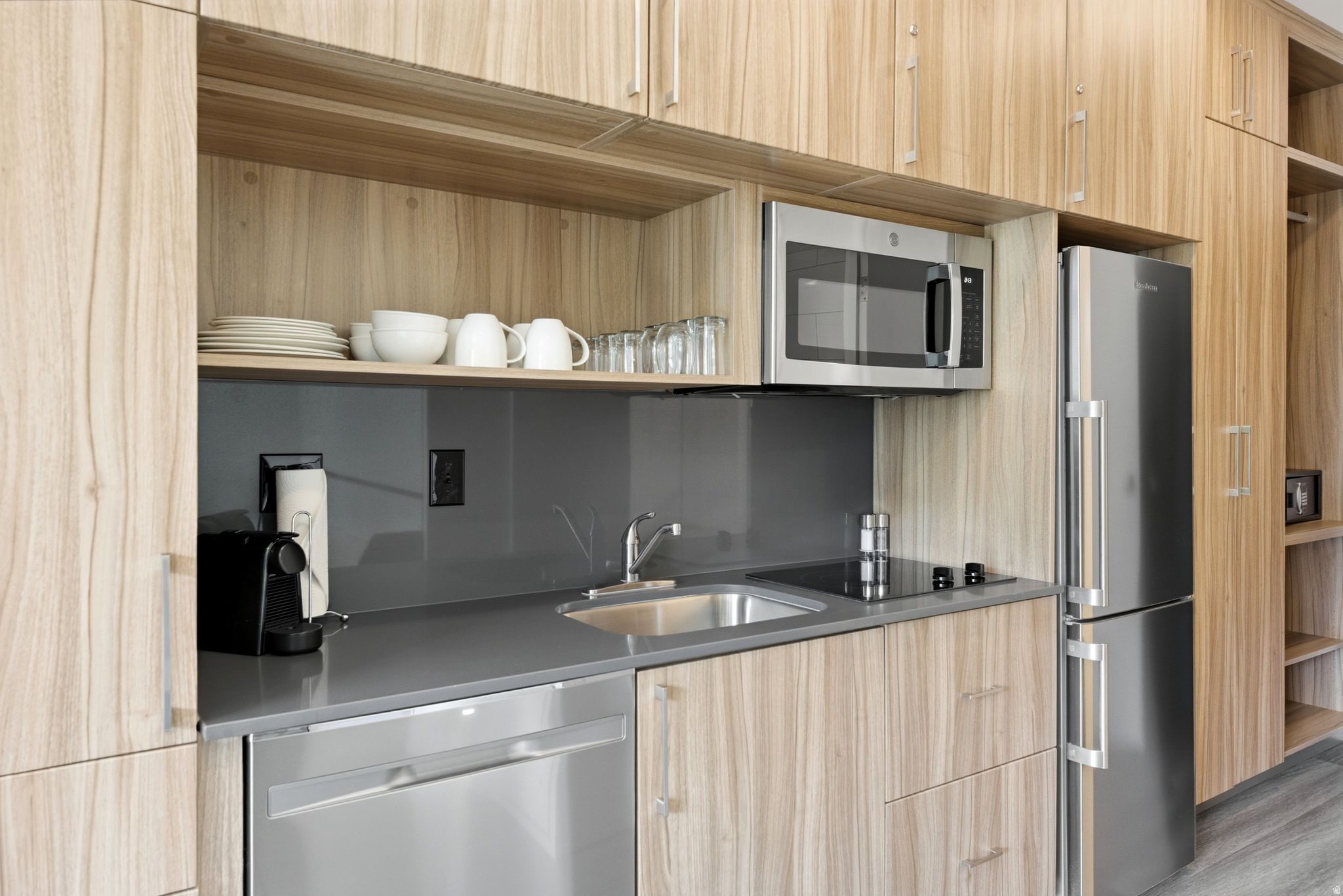 Compact kitchen area featuring wood-finish cabinetry, stainless steel appliances, a built-in microwave, an integrated cooktop, and a stainless steel sink