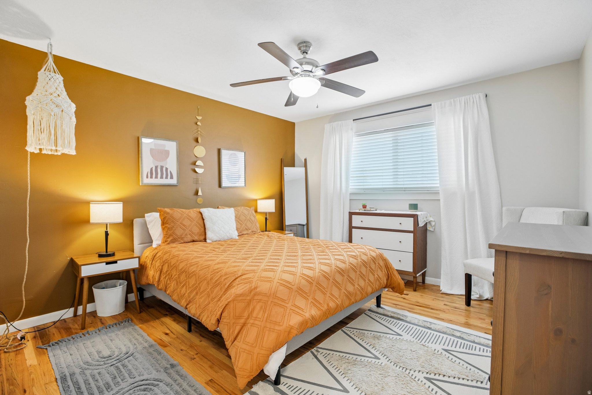 Bedroom featuring a ceiling fan, wood-finish flooring, a window with blinds, and an accent wall