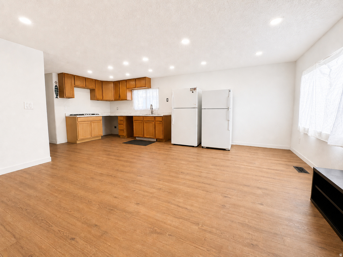 Open-concept kitchen and living area featuring wood-finish flooring, recessed lighting, and a white color palette